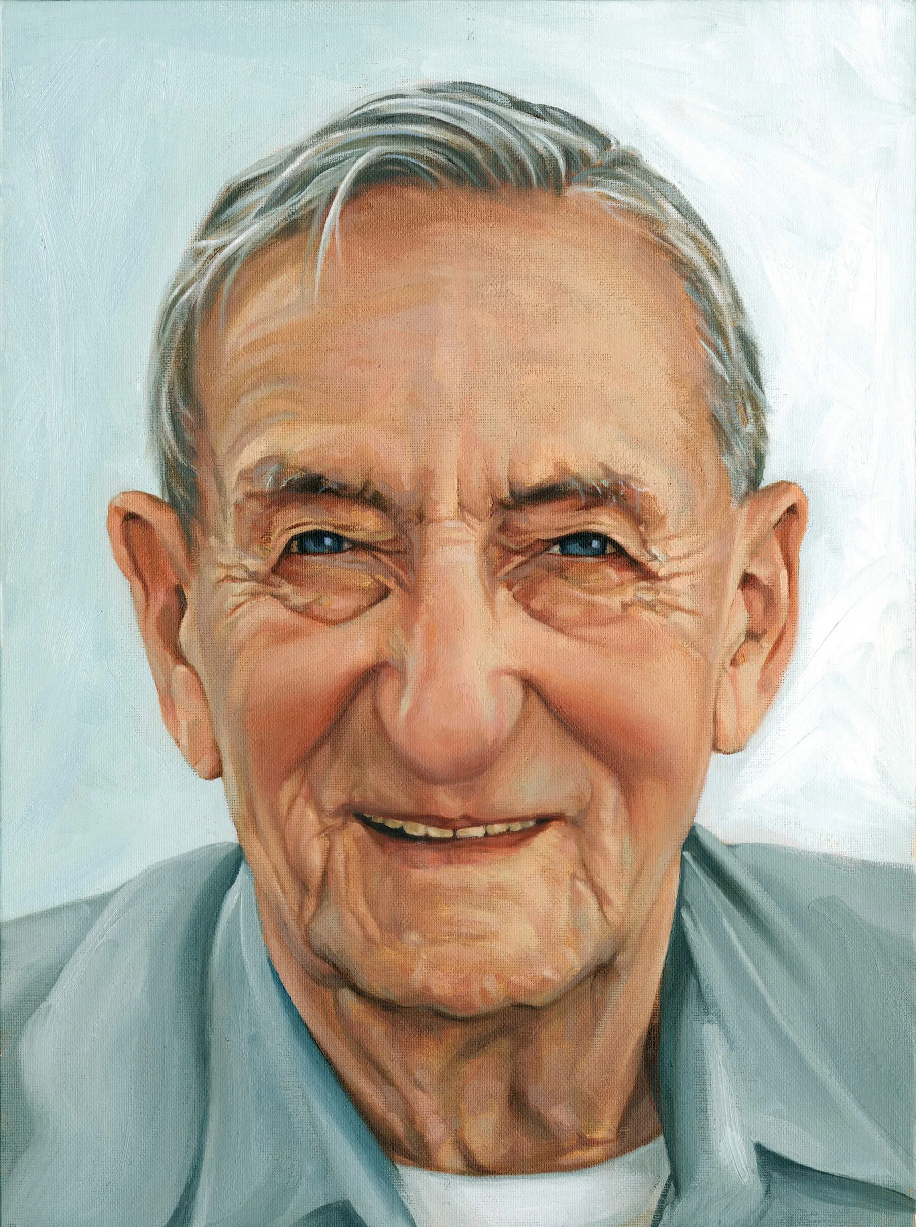 Close-up of an elderly man with gray hair, wearing glasses, smiling, dressed in a blue shirt and gray blazer.