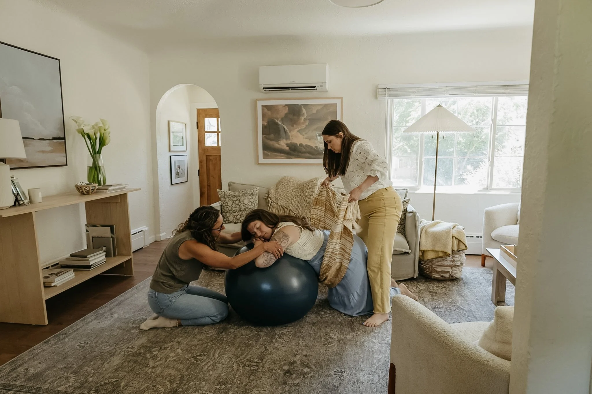 A group of women participating in a childbirth education class, practicing labor positions with a birthing ball in a living room.
