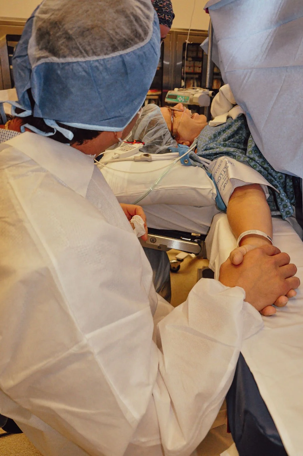 A healthcare professional and a patient holding hands during a medical procedure in a hospital room.
