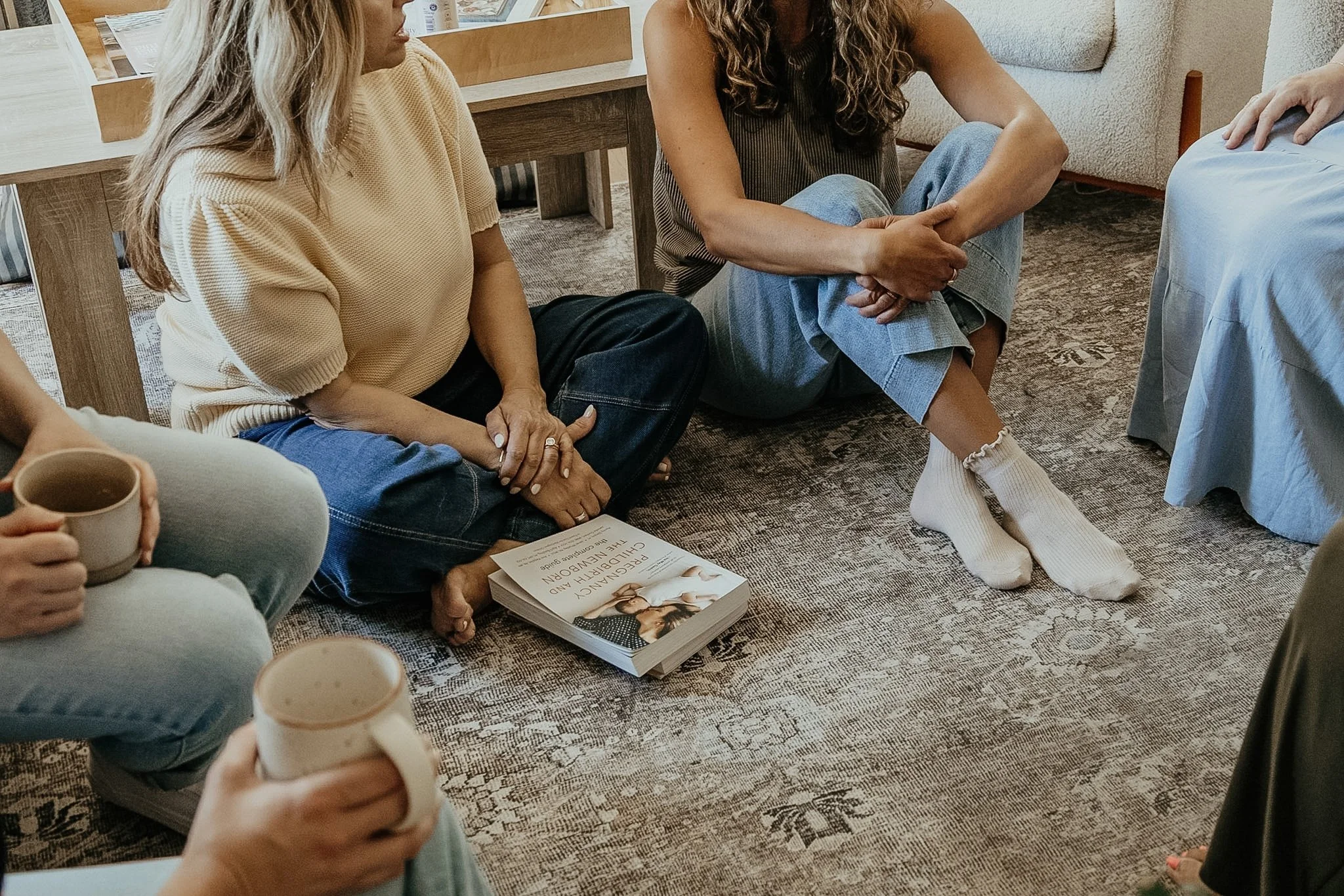 People sitting on the floor in a circle during a discussion, with books and coffee mugs nearby.