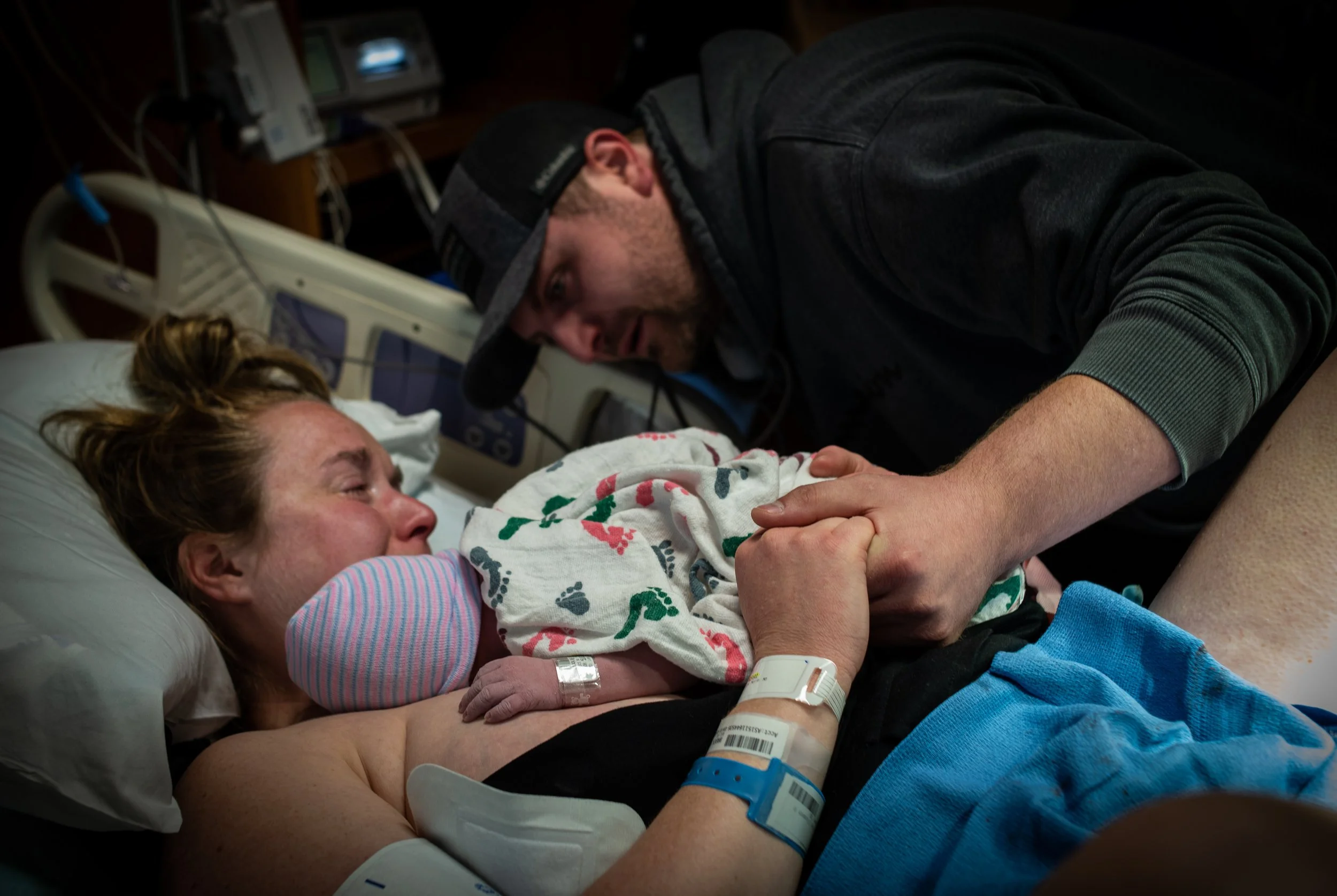 A woman lying in a hospital bed with IVs, holding hands with a man leaning over her, both appearing emotional.
