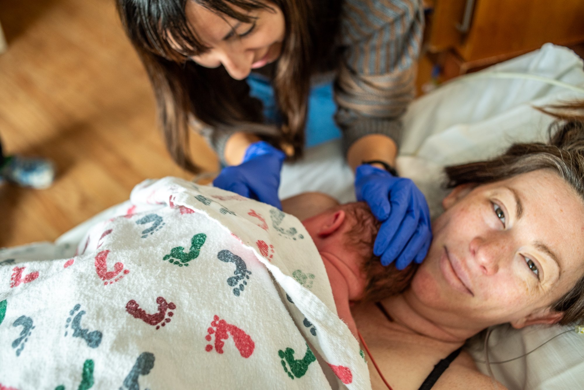 Woman giving birth to a baby in a hospital bed with support from a nurse or midwife.