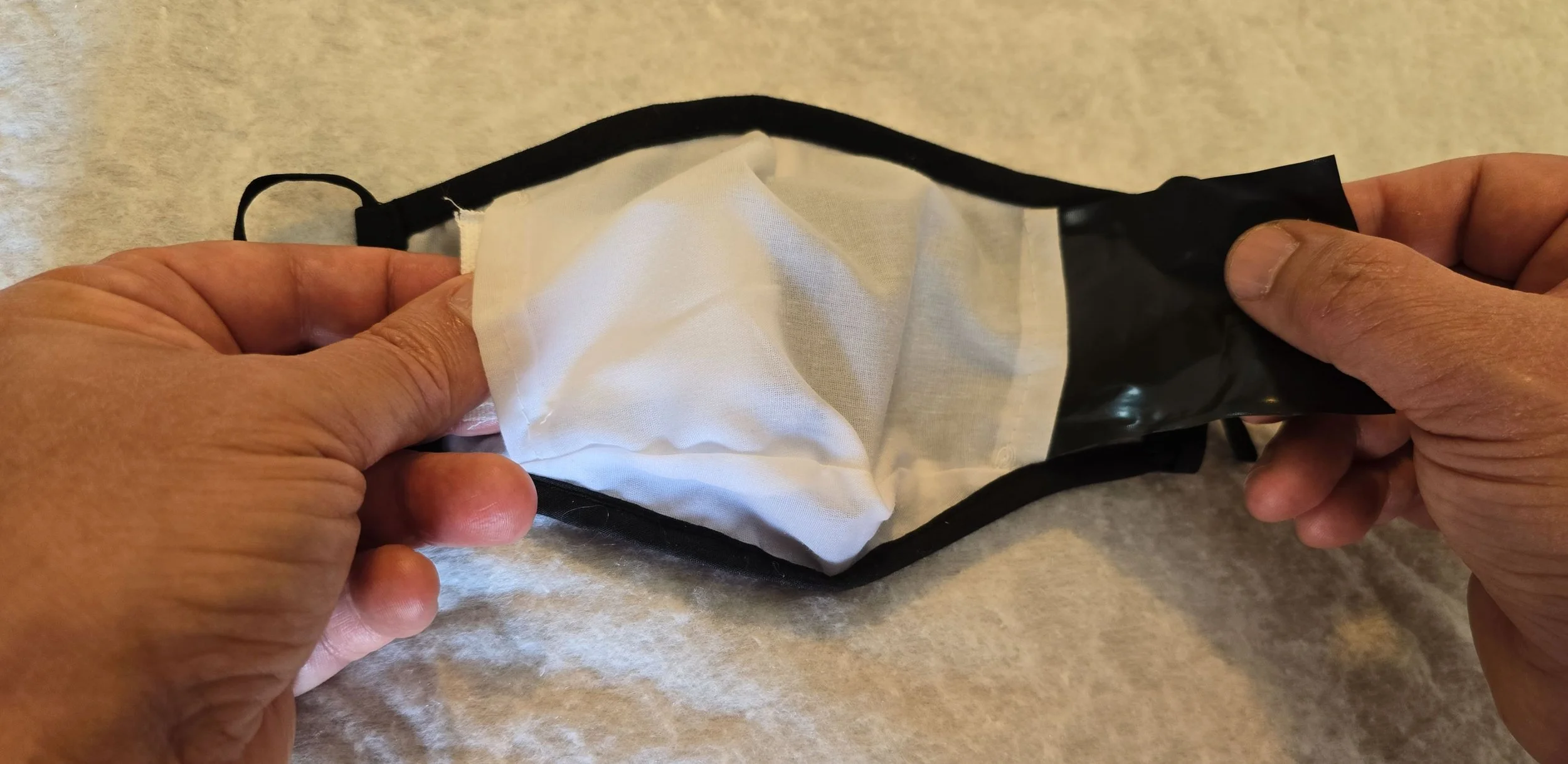 Person holding a partially opened black and white face mask with cloth inside, on a countertop