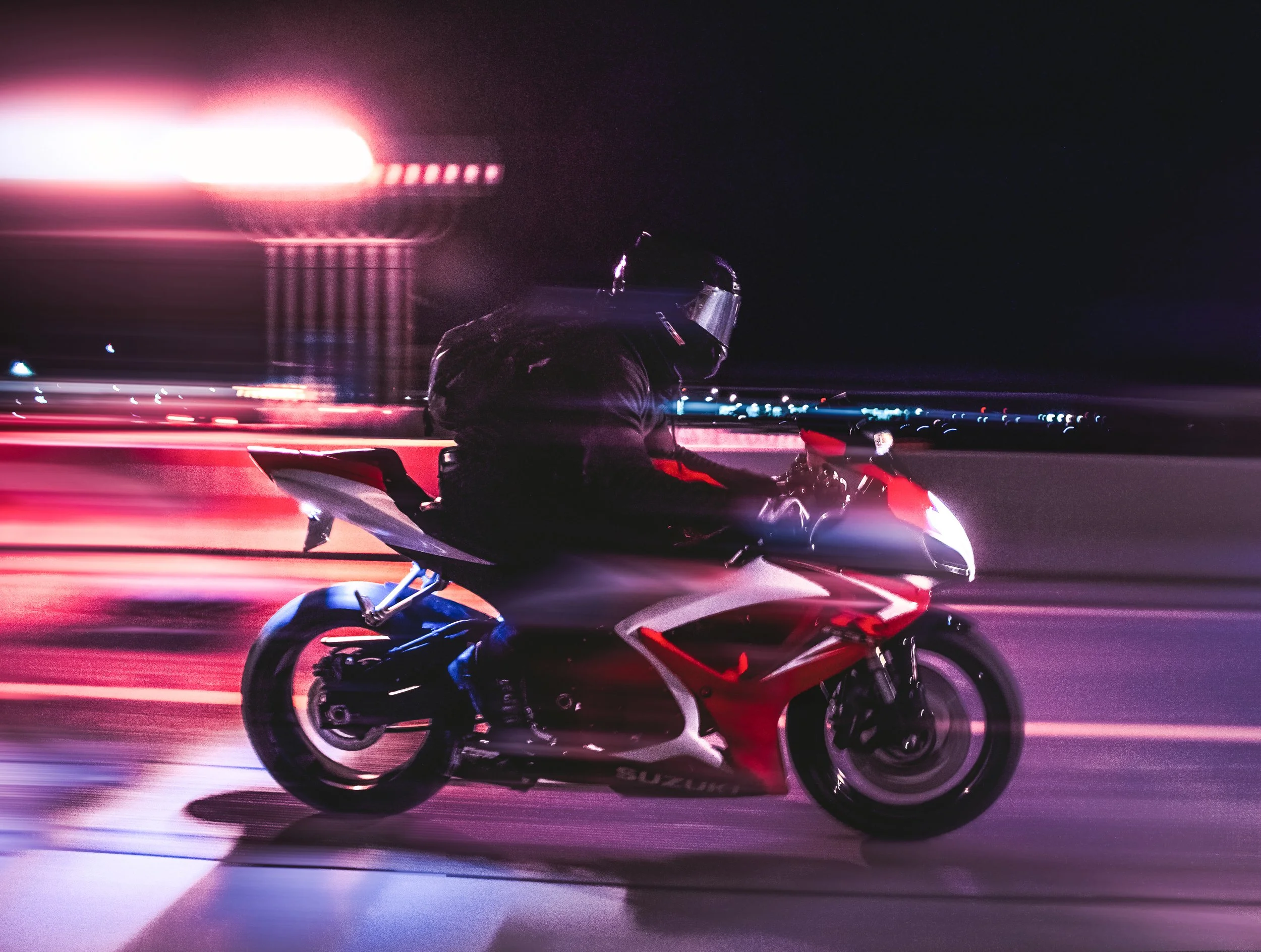 A person riding a red and white motorcycle at night with blurred city lights in the background.
