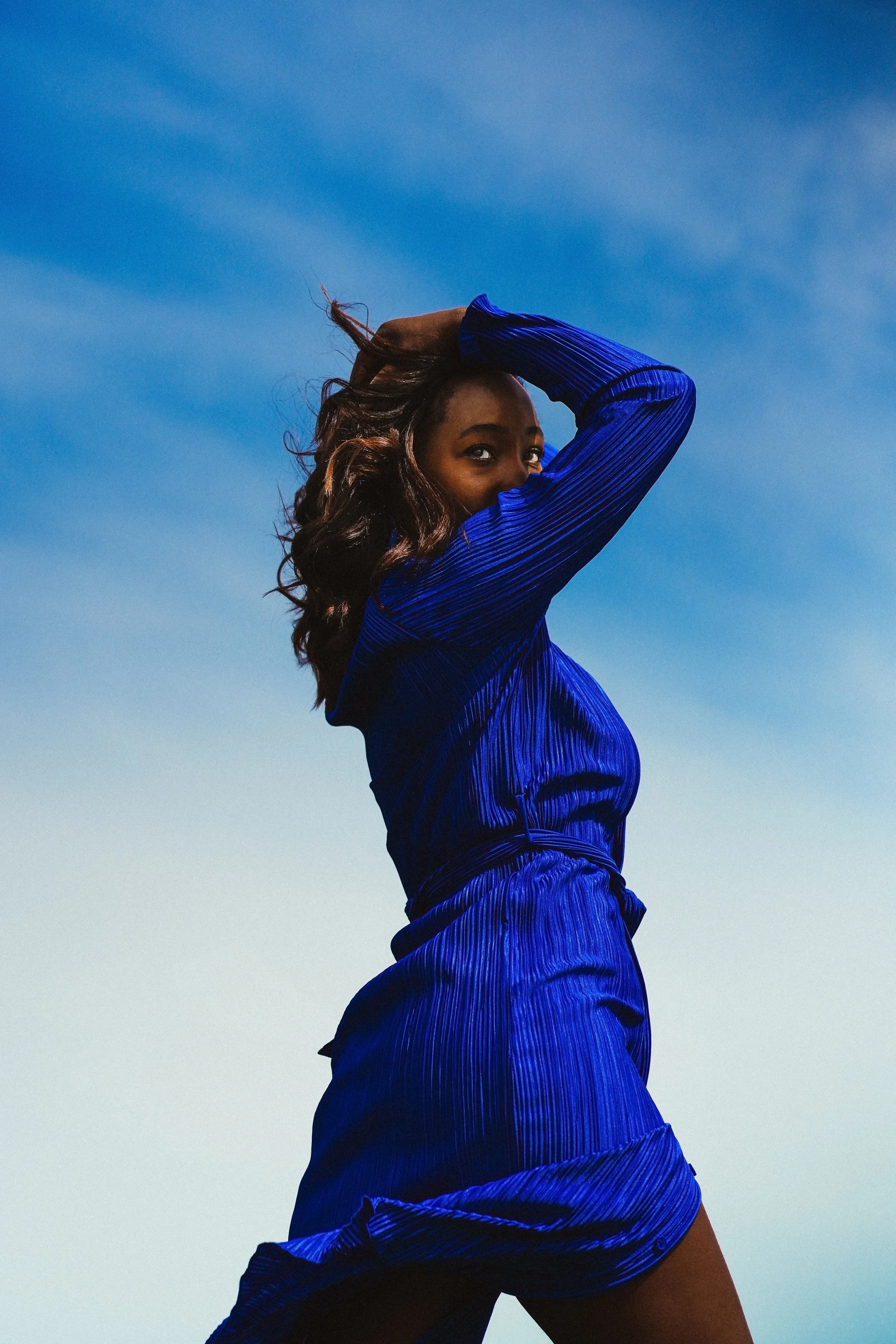 A woman in a blue dress posing outdoors against a clear blue sky.