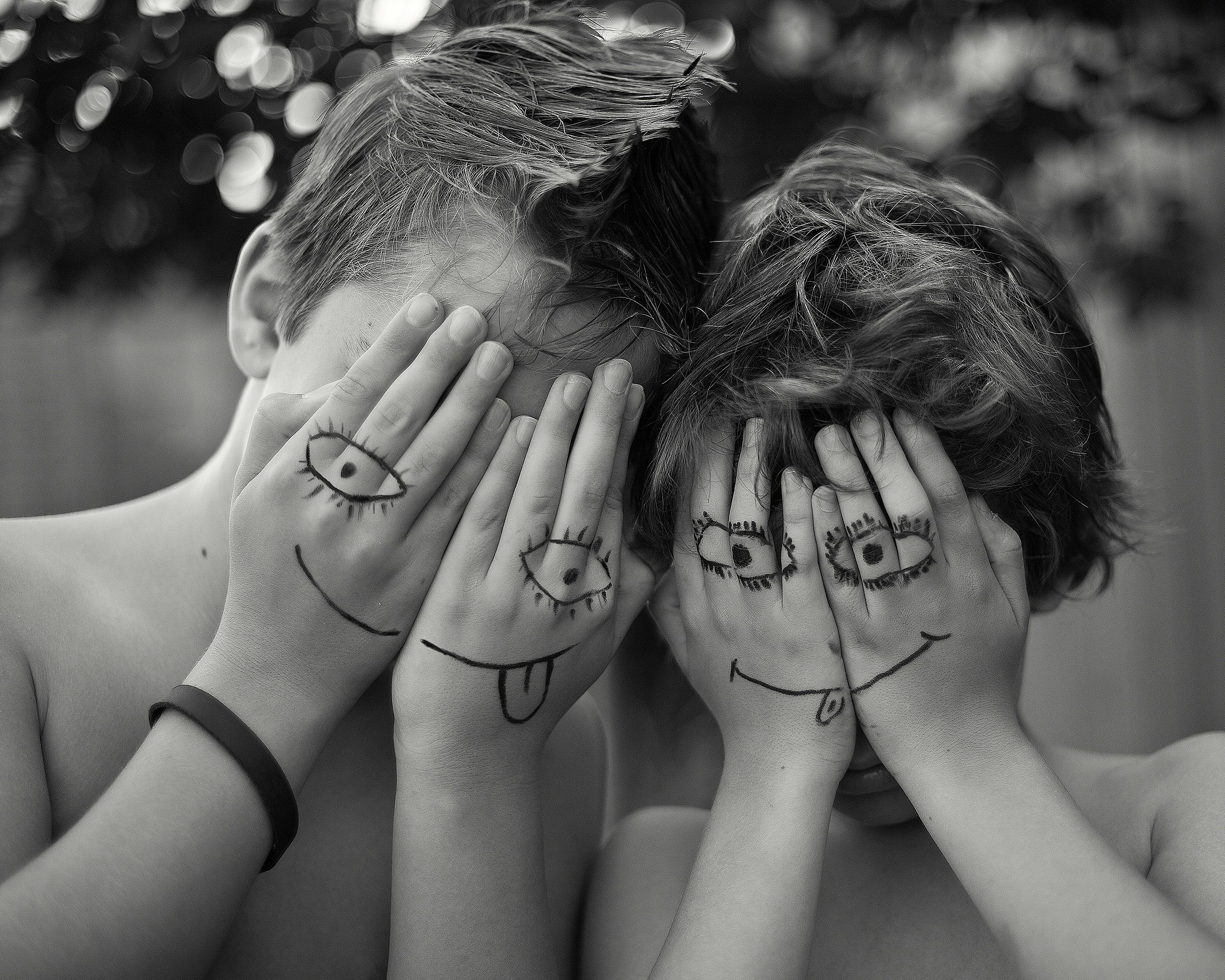 Groupe de mains d'enfants avec des dessins de visages et d'yeux tracés sur la peau, posées ensemble. L'image est en noir et blanc, floue d'arrière-plan.
