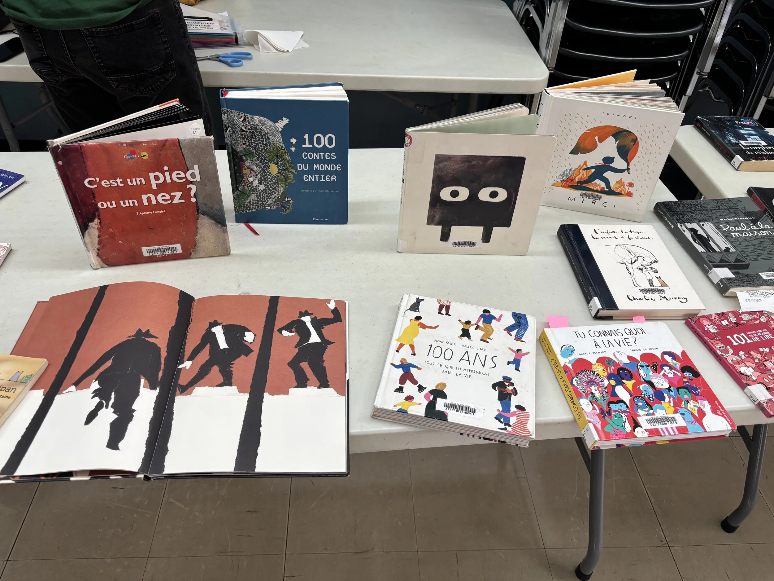 Une table avec plusieurs livres empilés, dont certains ont des dessins et des titres en français, dans un environnement intérieur.