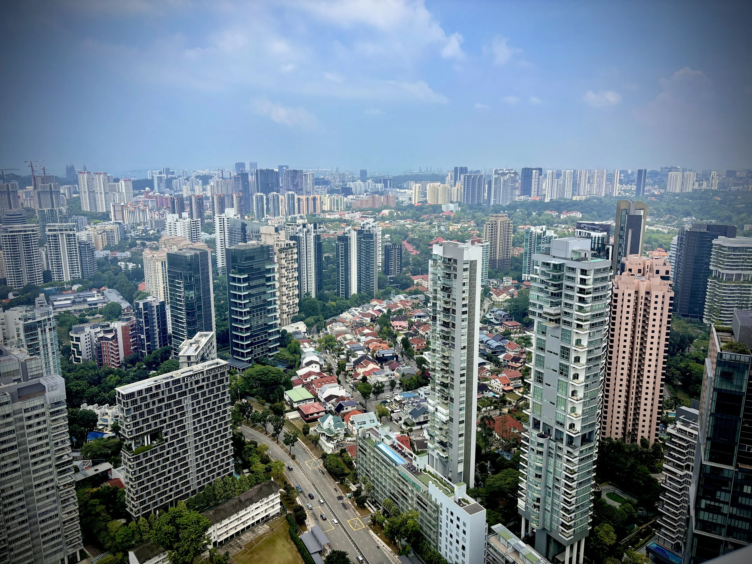 A city skyline with numerous high-rise buildings, residential and commercial structures, and a cloudy sky overhead.