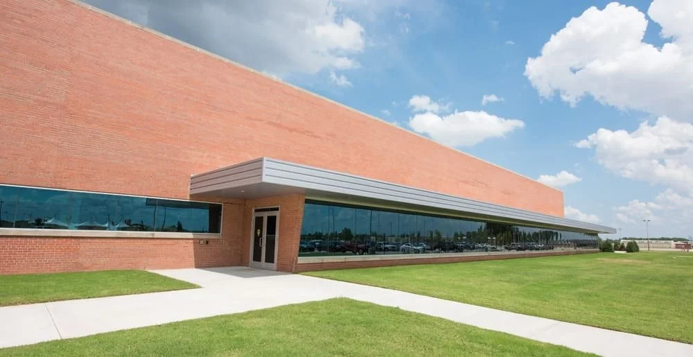 Modern brick building with large tinted glass windows and a metal awning under a partly cloudy sky.