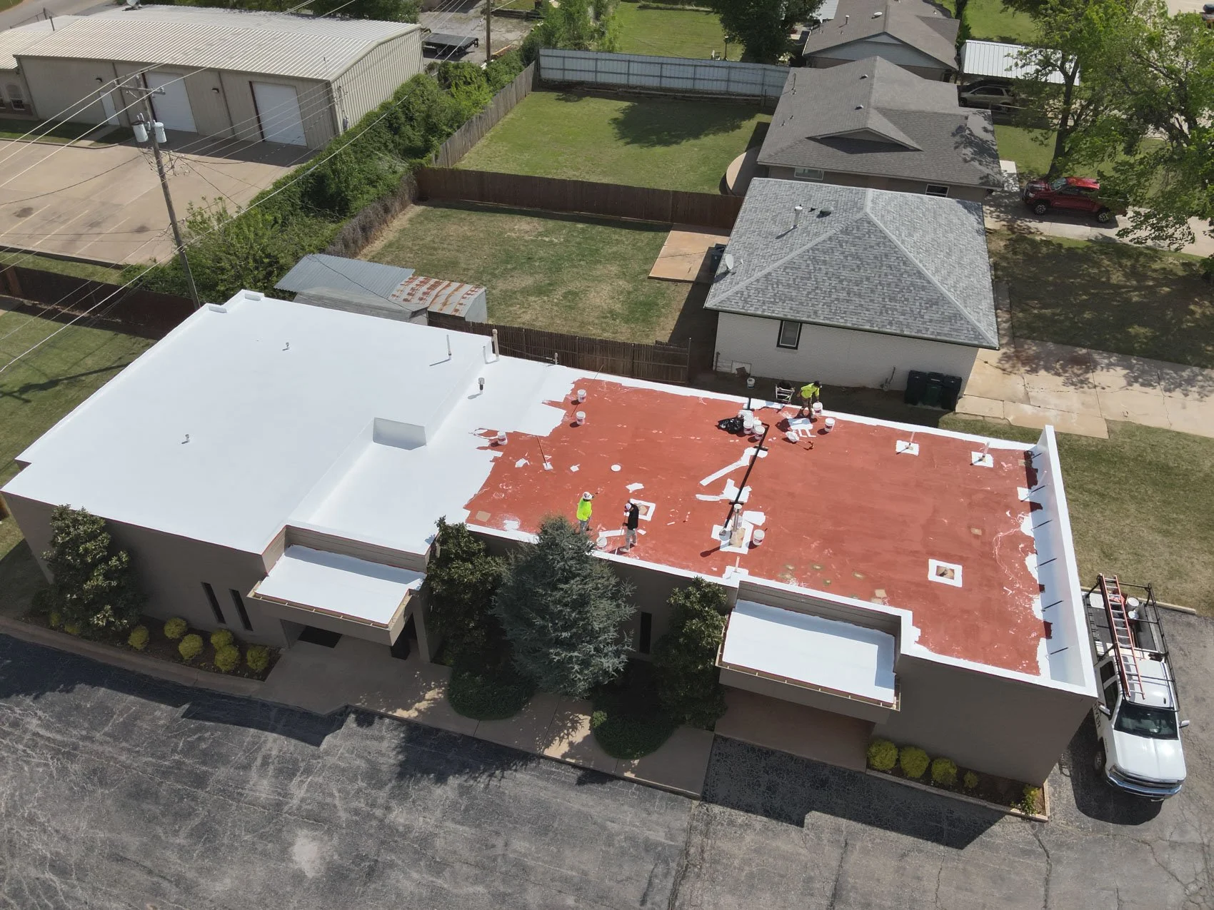 Aerial view of a house under construction, with workers working on the roof, which is partially covered with red roofing material and white patches.