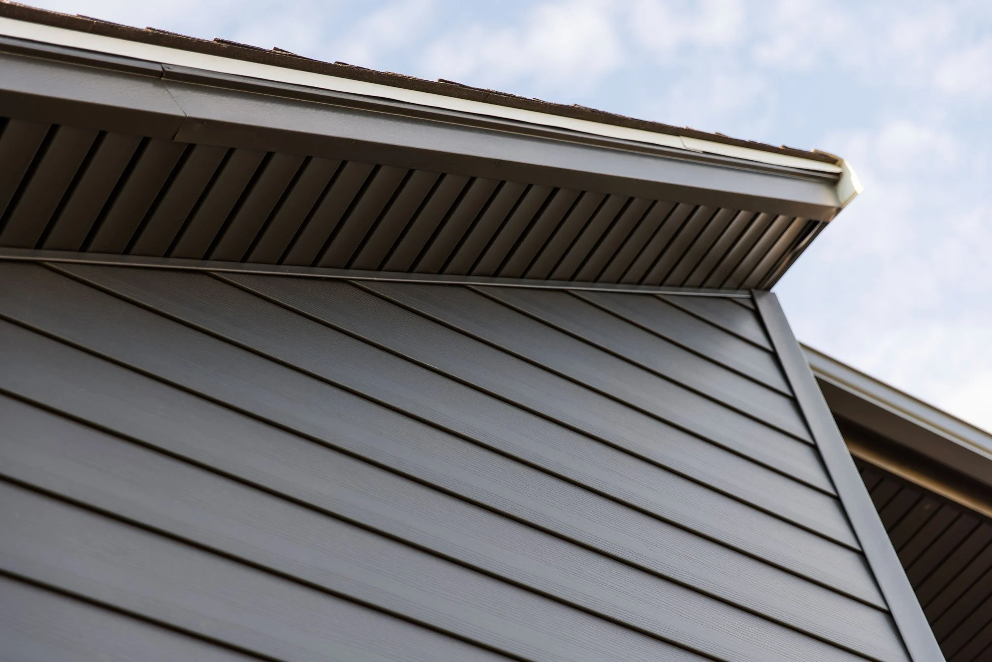 Close-up of the soffit and the overhanging roof of a house, showing horizontal siding and attic venting.