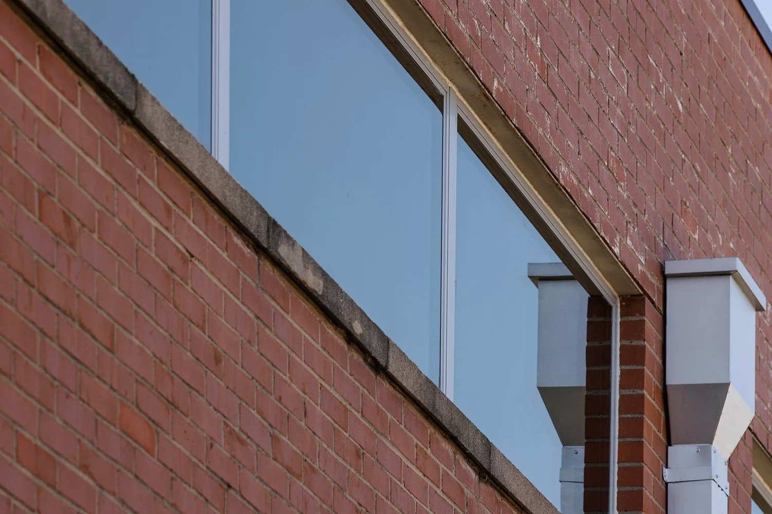 Close-up of a brick building with a large window and an exterior vent pipe.