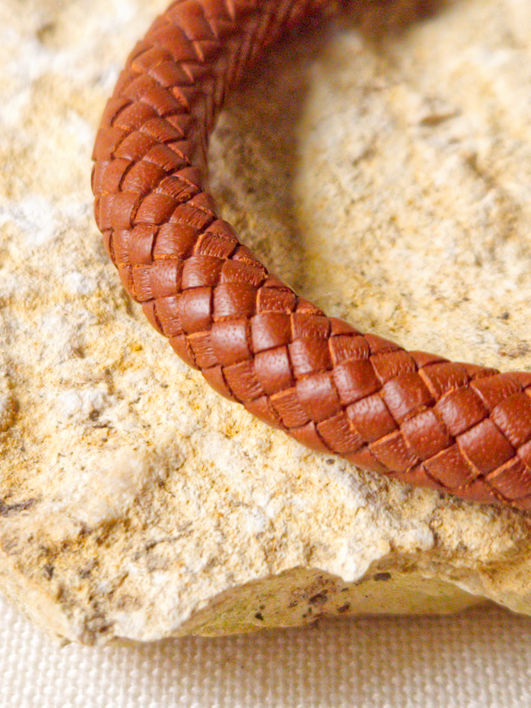 Close-up of a braided bracelet resembling a woven pattern, on a white textured surface.