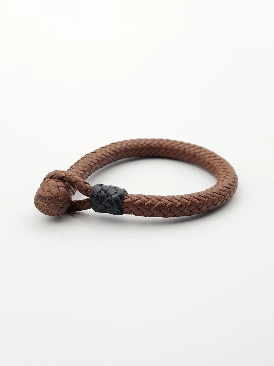 Brown braided leather bracelet with a black accent knot, placed on a white surface.
