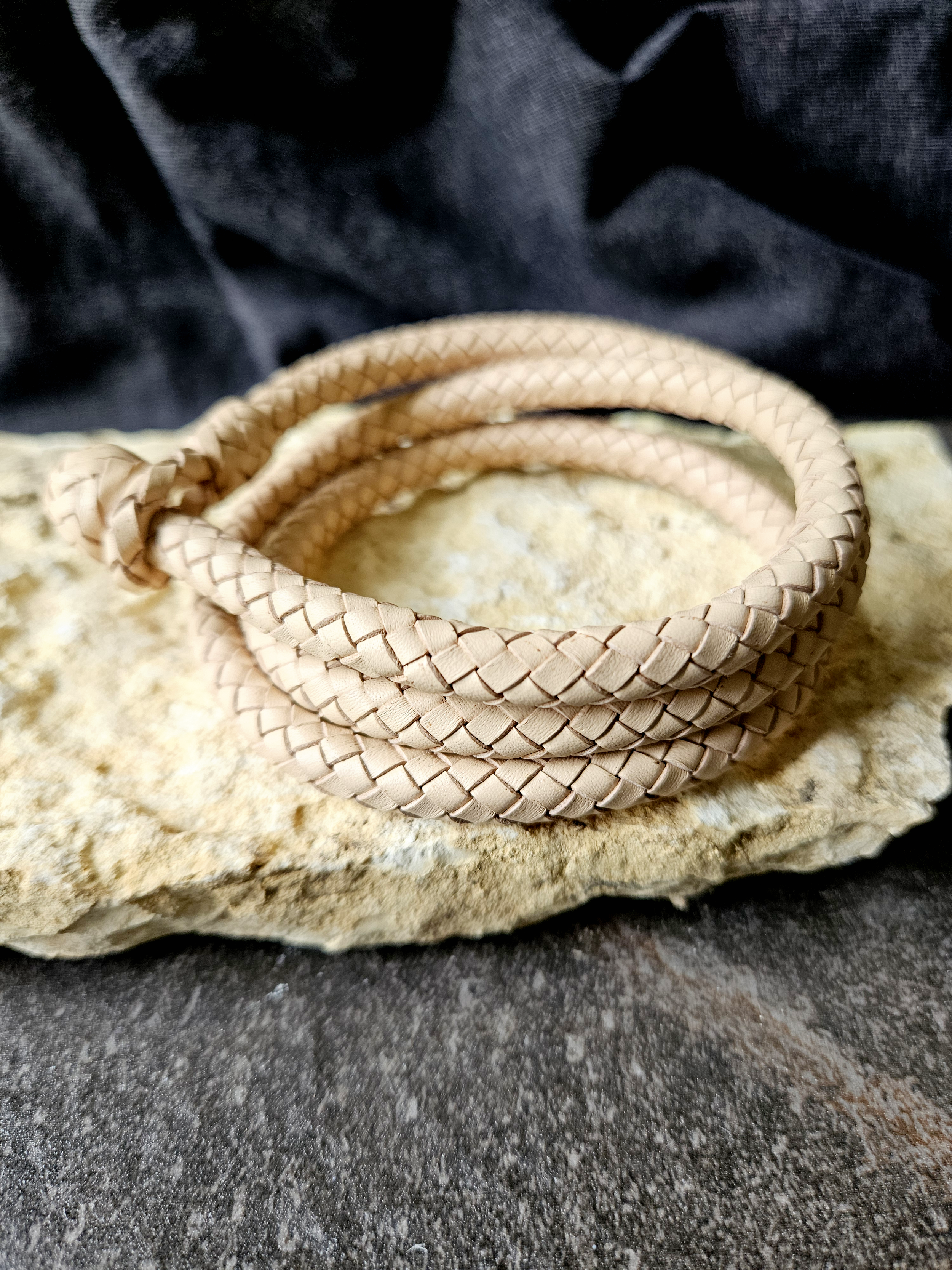 A coiled bracelet resting on a rough, dark stone surface with black fabric in the background.