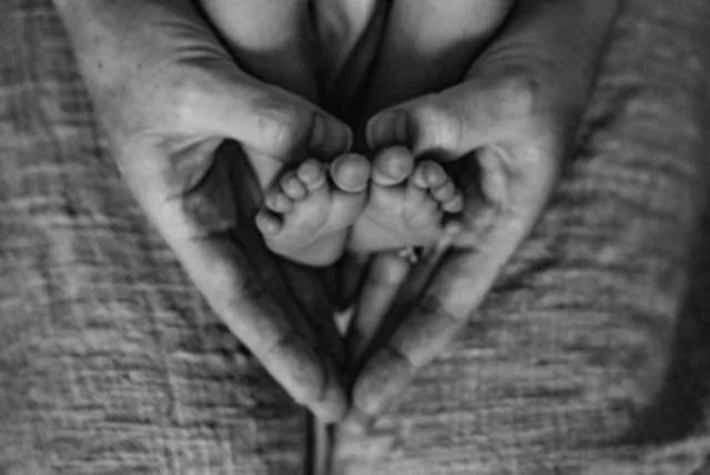 A pair of adult hands forming a heart shape around small baby feet.