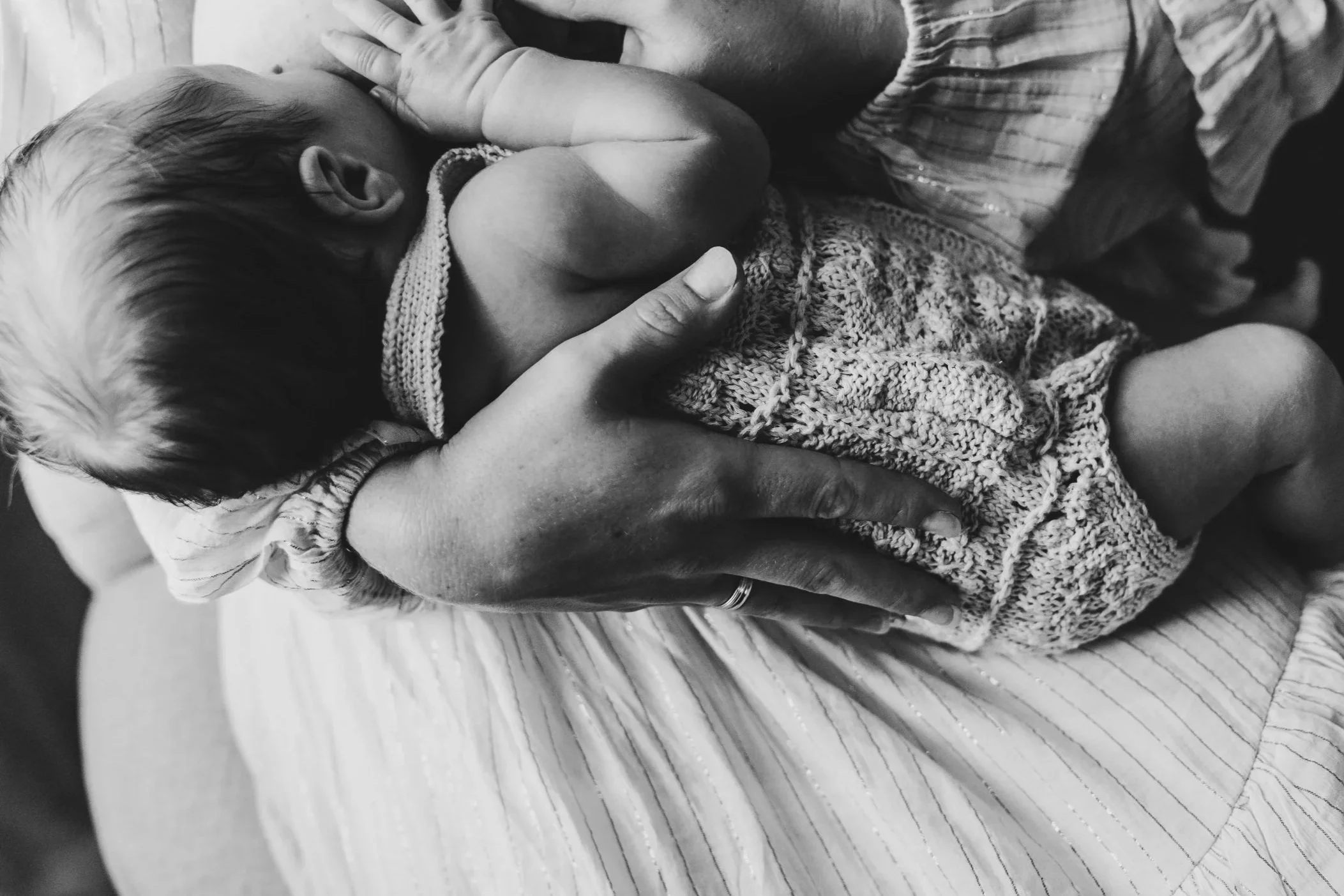 A newborn baby being cradled in an adult's hands, with the baby wrapped in a knitted blanket.