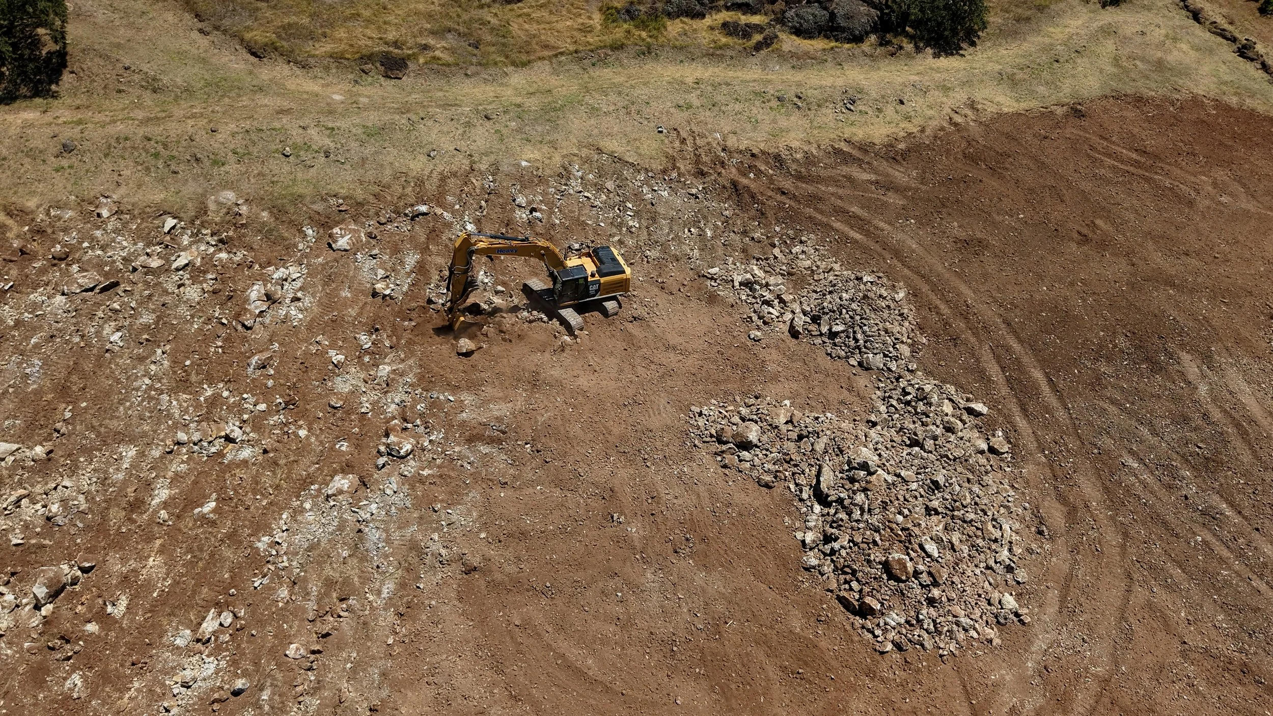 CAT 336 Excavator moving large rocks and earth in an open field. Land preparation for vineyard development. Rock Removal. Soil Preparation