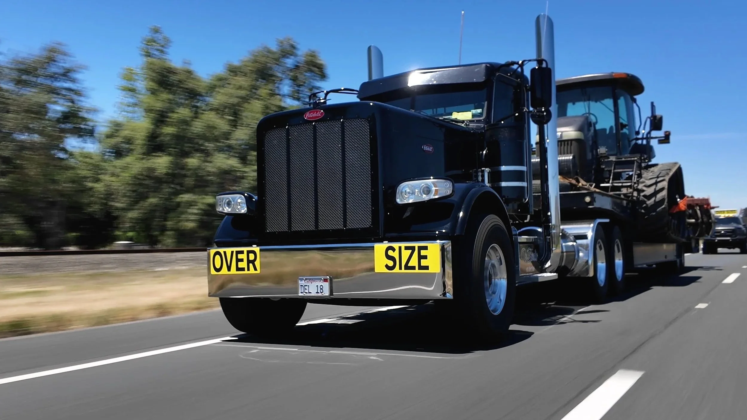 Black Peterbilt semi-truck with a chrome bumper and yellow 'Over Size' signs on the front. Heavy Equipment hauling Experts Northern California
