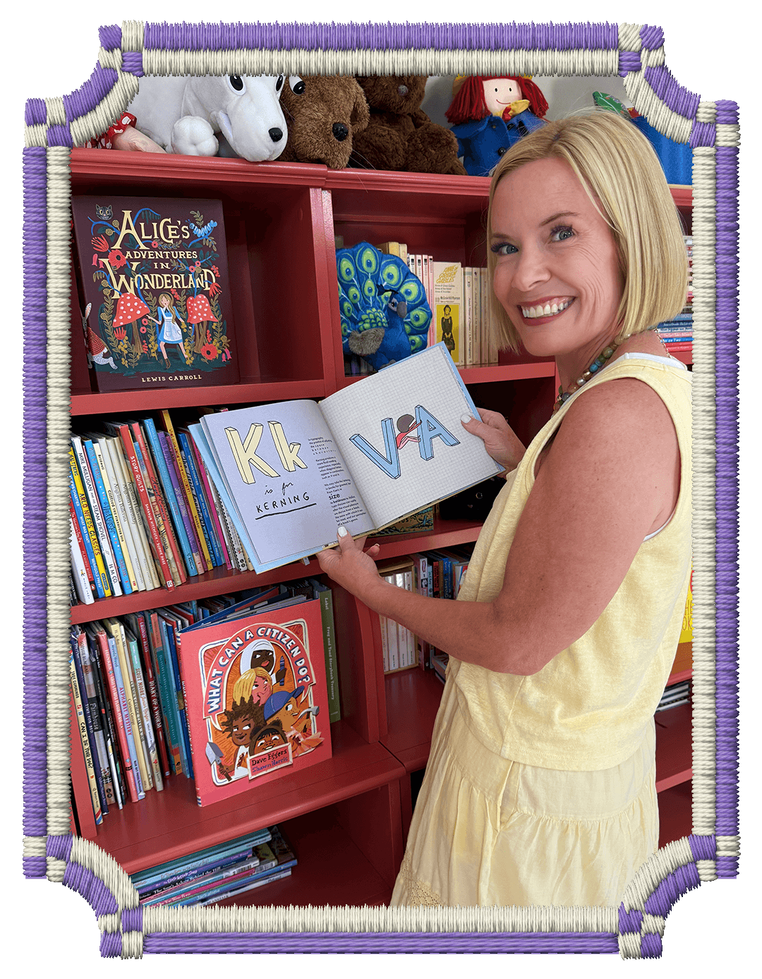 Rachel Smalley smiling while holding a children's alphabet book, in a colorful library filled with children's books and plush toys.