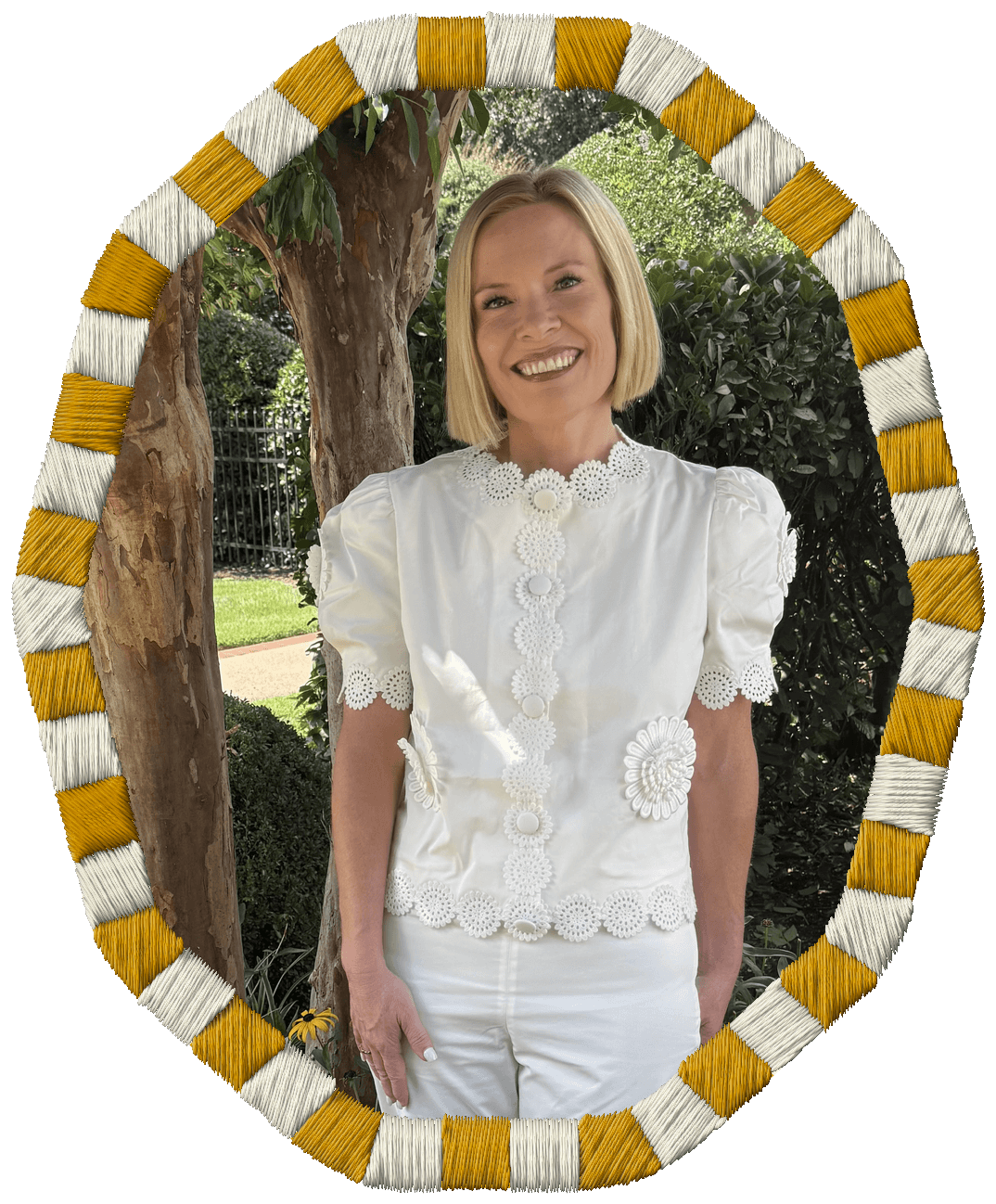 Rachel Smalley with short blonde hair smiling, wearing a white embroidered top, standing outdoors in front of trees and greenery.