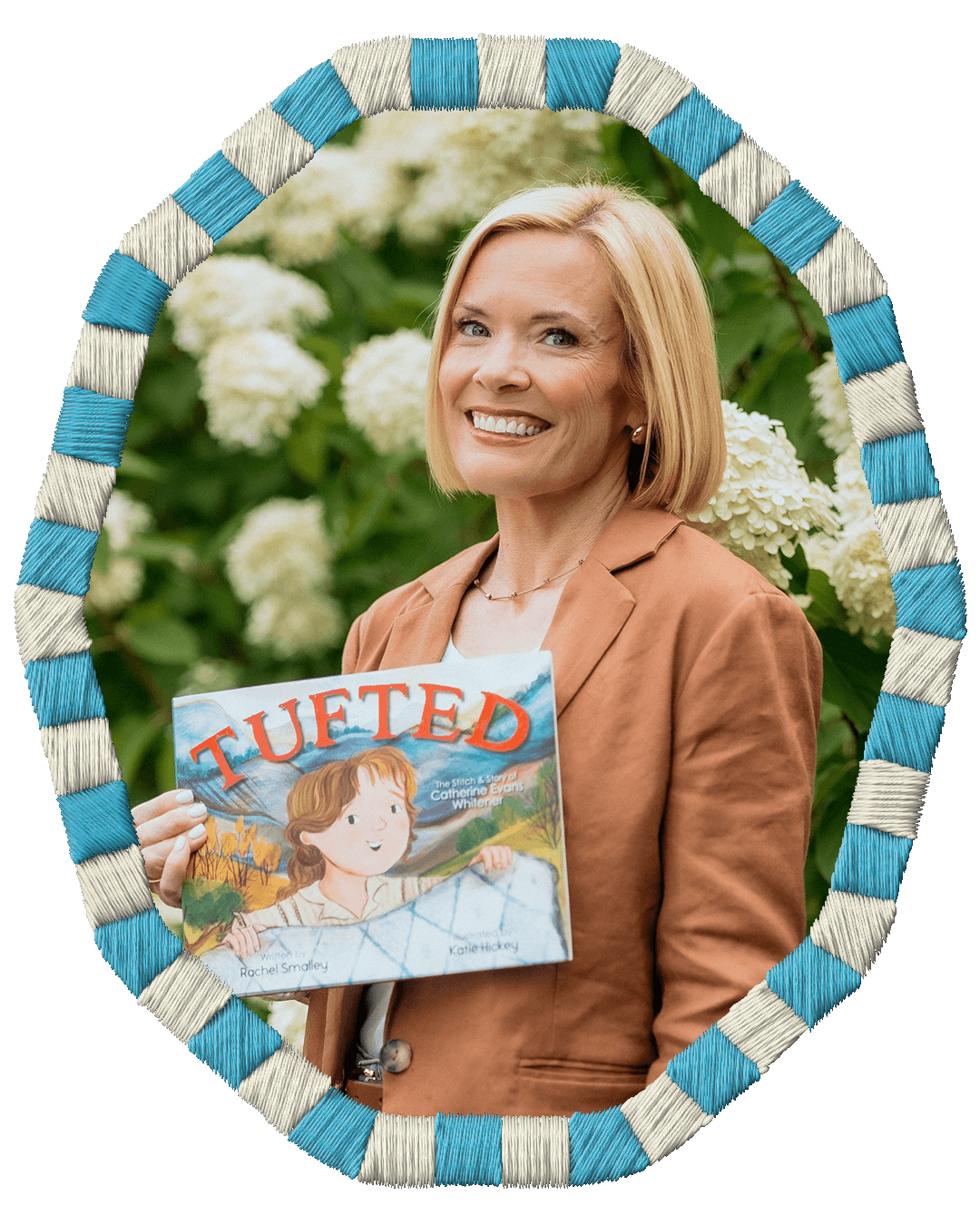 Rachel Smalley holding a children's book titled 'TUFTED' stands outdoors with green foliage and white hydrangea flowers in the background. She is smiling and wearing a brown blazer.