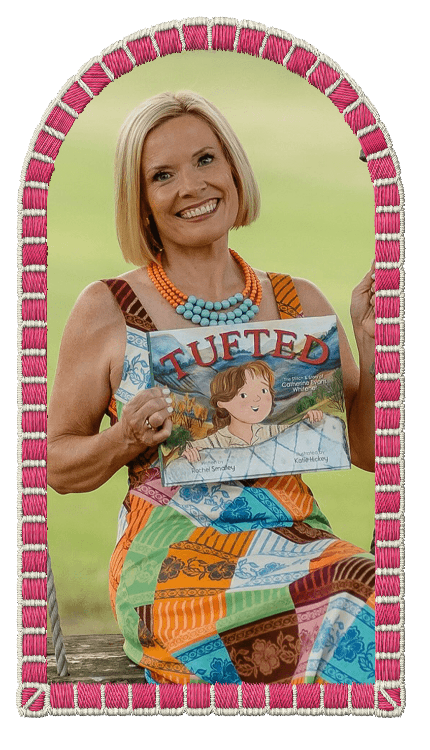 Rachel Smalley with blonde hair wearing a colorful dress and multicolored beaded necklaces, holding a children's book titled 'TUFTED,' smiling at the camera, with a plain green background and a decorative pink and white embroidered border.