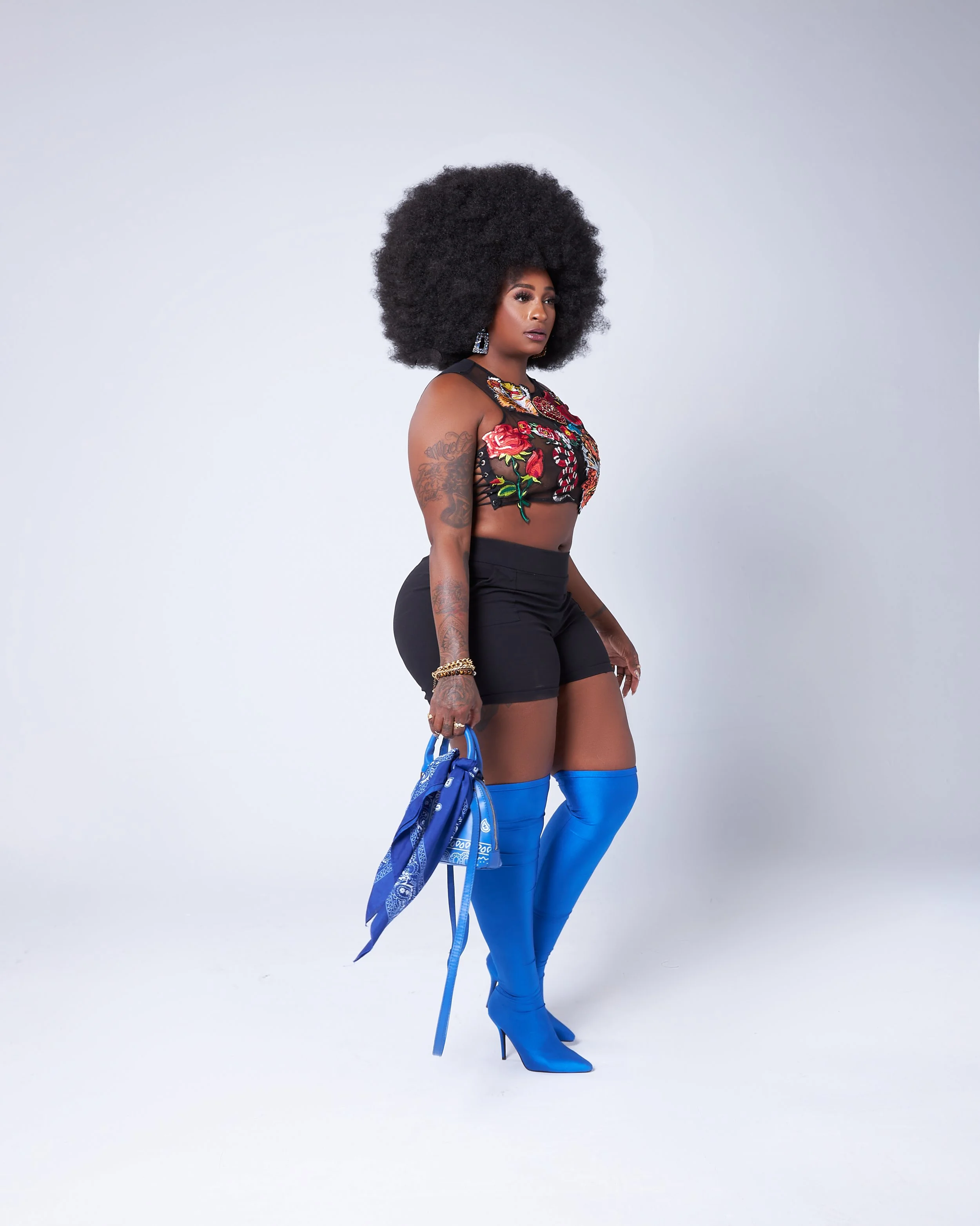 Woman with dark curly hair in a floral crop top and high heels in a studio shot.