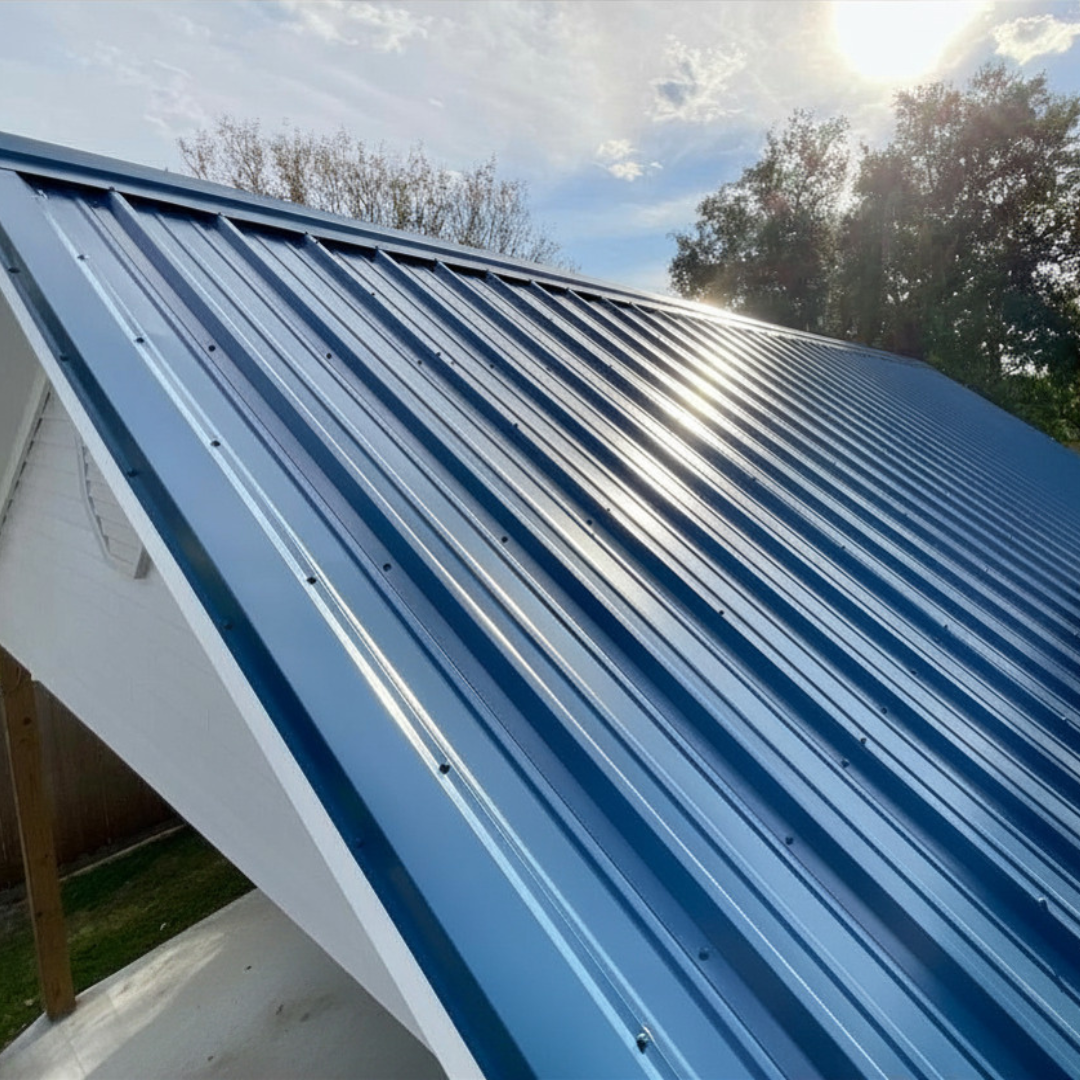 Close-up of a new blue metal roof on a house with sunlight reflecting off its surface and trees in the background.