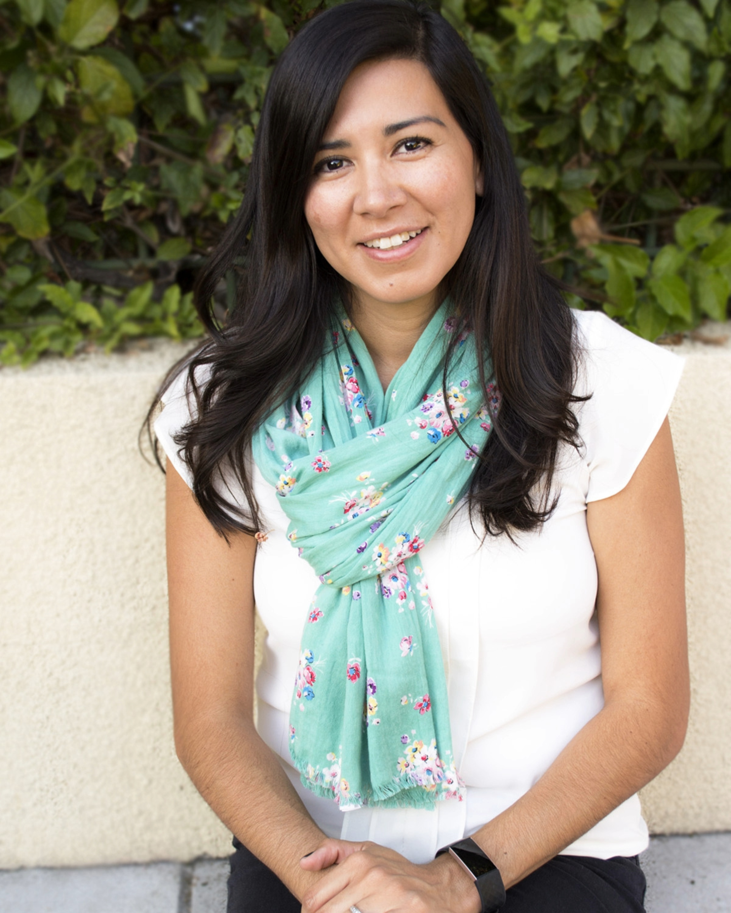 Headshot of Jacqueline S. Armes, LMFT, smiling outdoors in front of greenery, wearing a white top and teal floral scarf.
