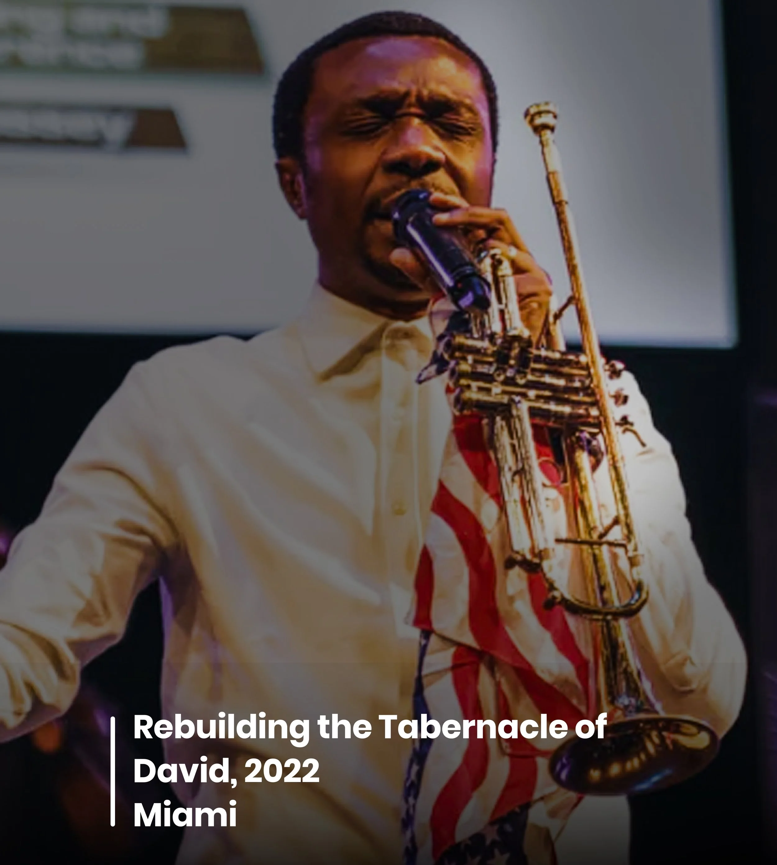 Close-up of a man with short black hair, singing into a microphone while holding a golden saxophone. He is wearing a white shirt and standing in front of a blurred background with text overlay about rebuilding the tabernacle of David, 2022 Miami.