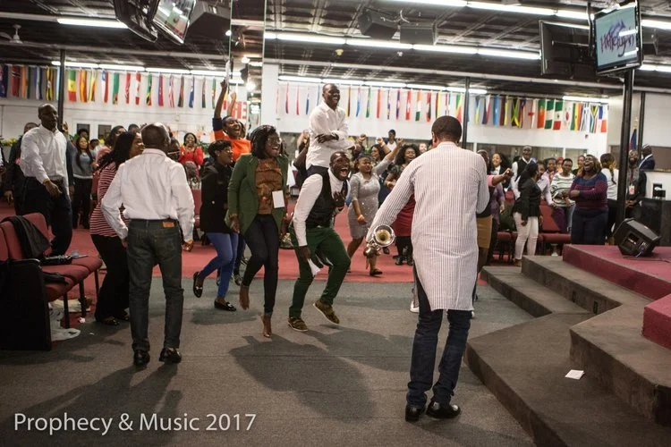 People dancing and enjoying music in a church or event hall with colorful flags hanging above.
