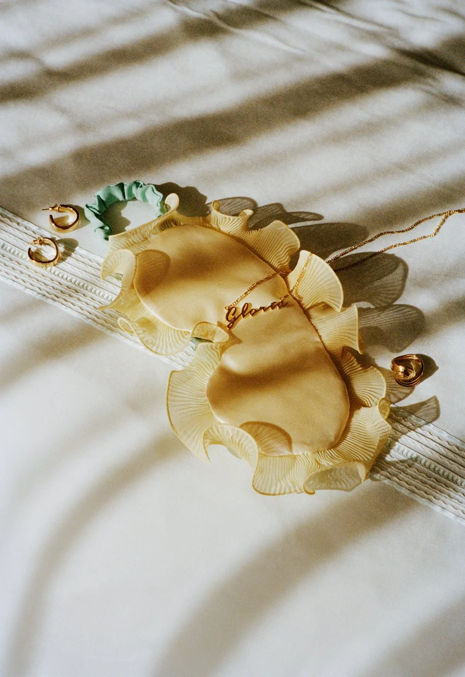 Gold necklace with a word pendant, gold earrings, and decorative shell-shaped jewelry on a white surface with soft shadows.