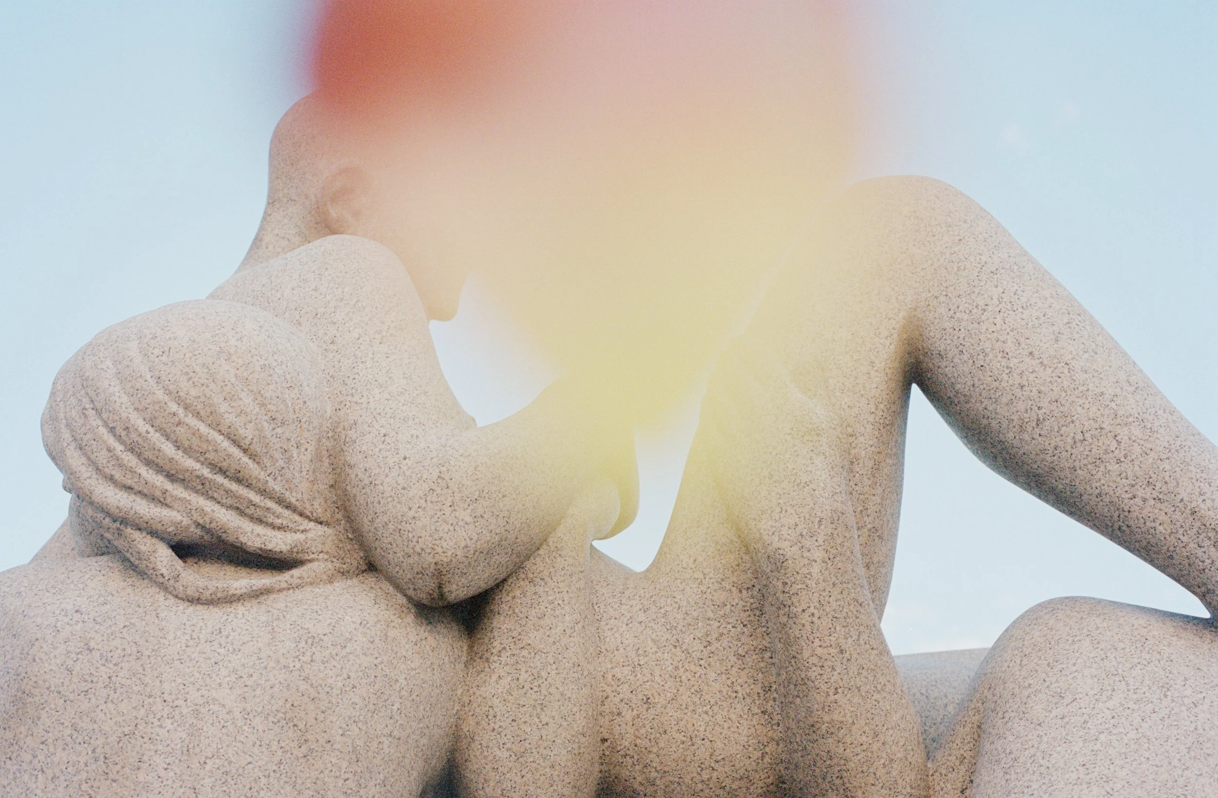 Close-up of a modern sculpture of two nude human figures, one leaning back and the other leaning forward, with a soft glow and blurred background.