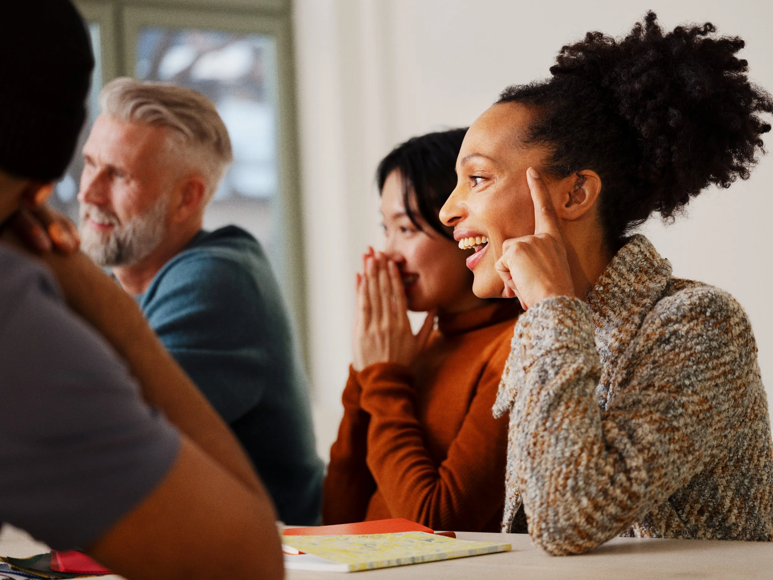 Group of diverse people sitting at a table, smiling and engaging in conversation.