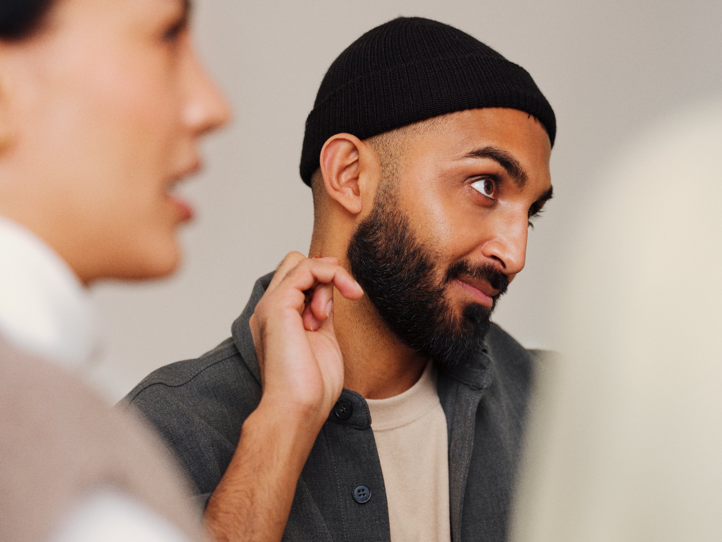 Close-up of a man with a beard wearing a black beanie and a dark shirt, looking attentively.