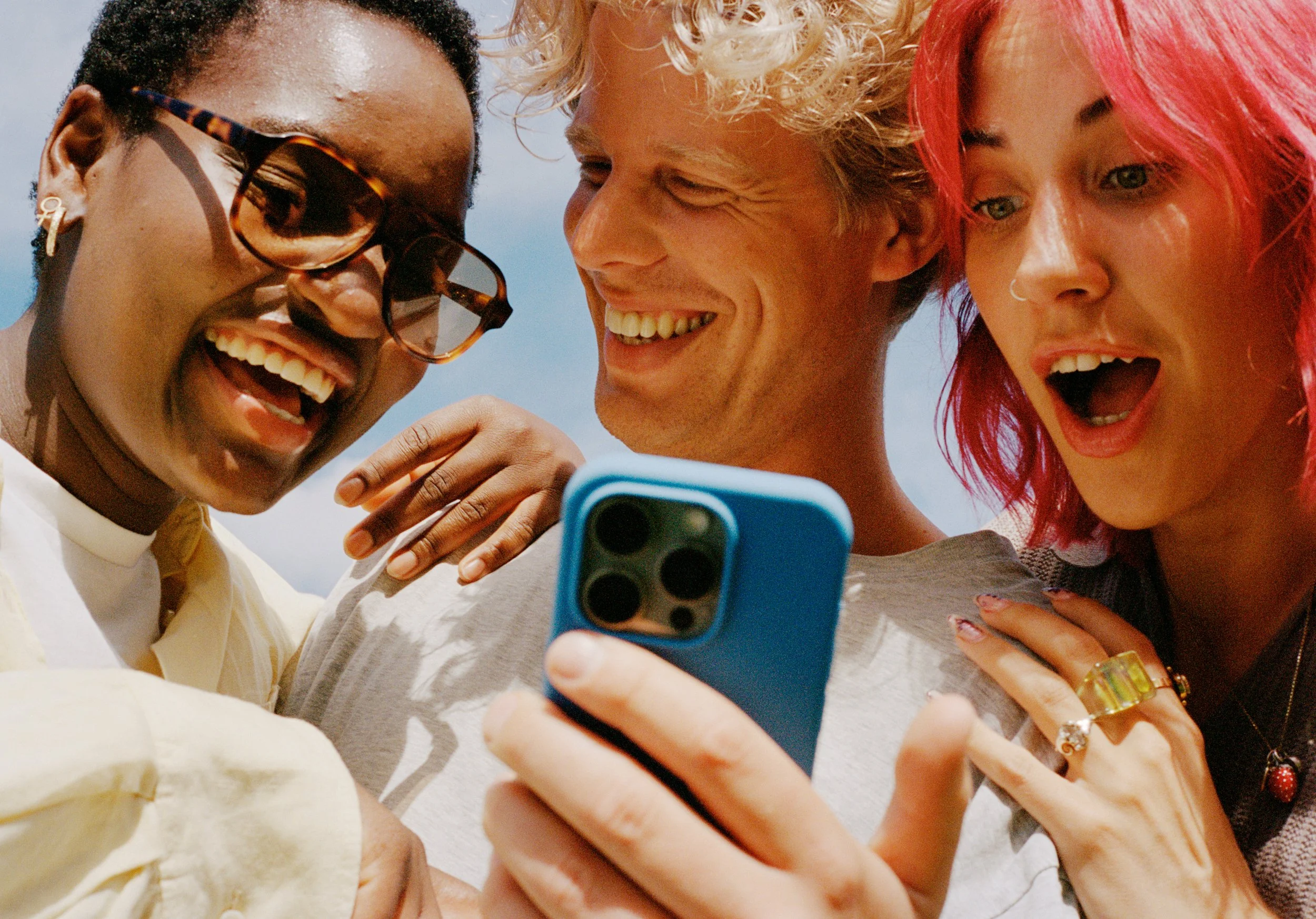Three friends smiling and looking at a phone together outside.