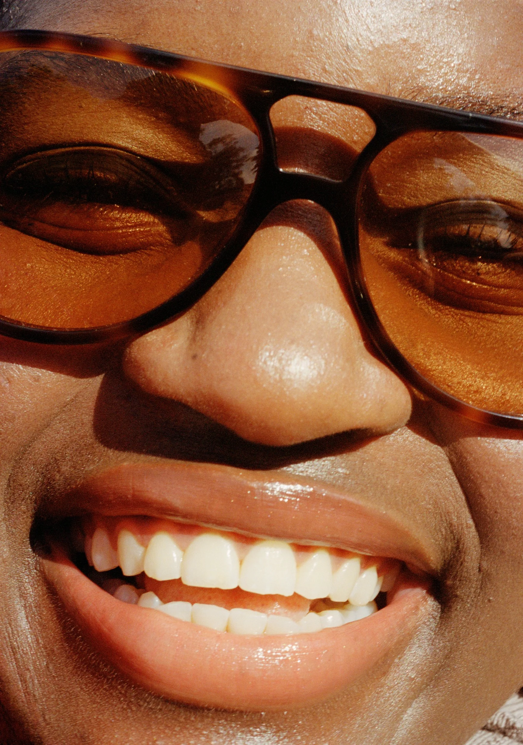 Close-up of a smiling person wearing large sunglasses, showing teeth and a joyful expression.