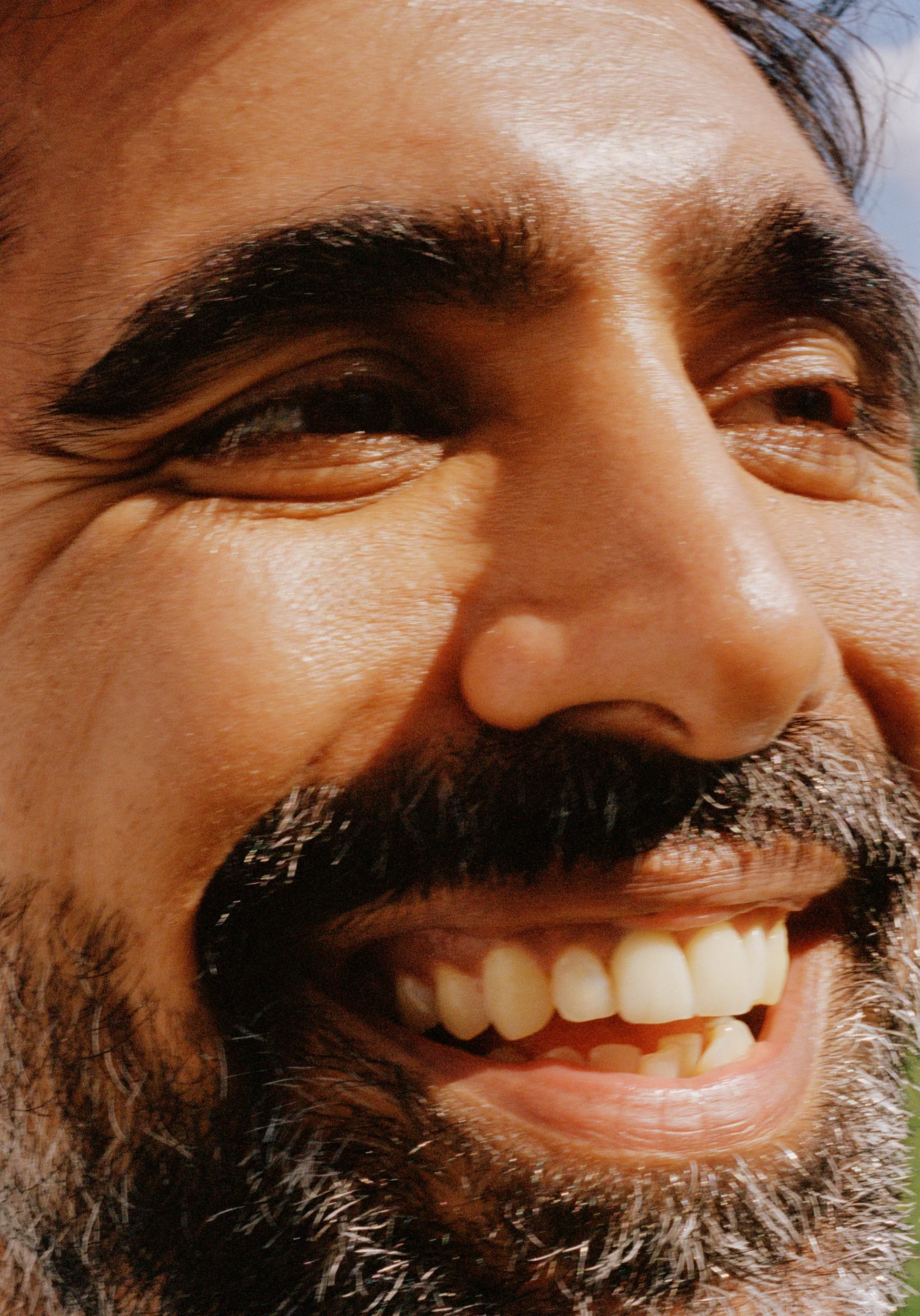 Close-up of a man's face showing a wide smile, with dark hair, likely taken outdoors.