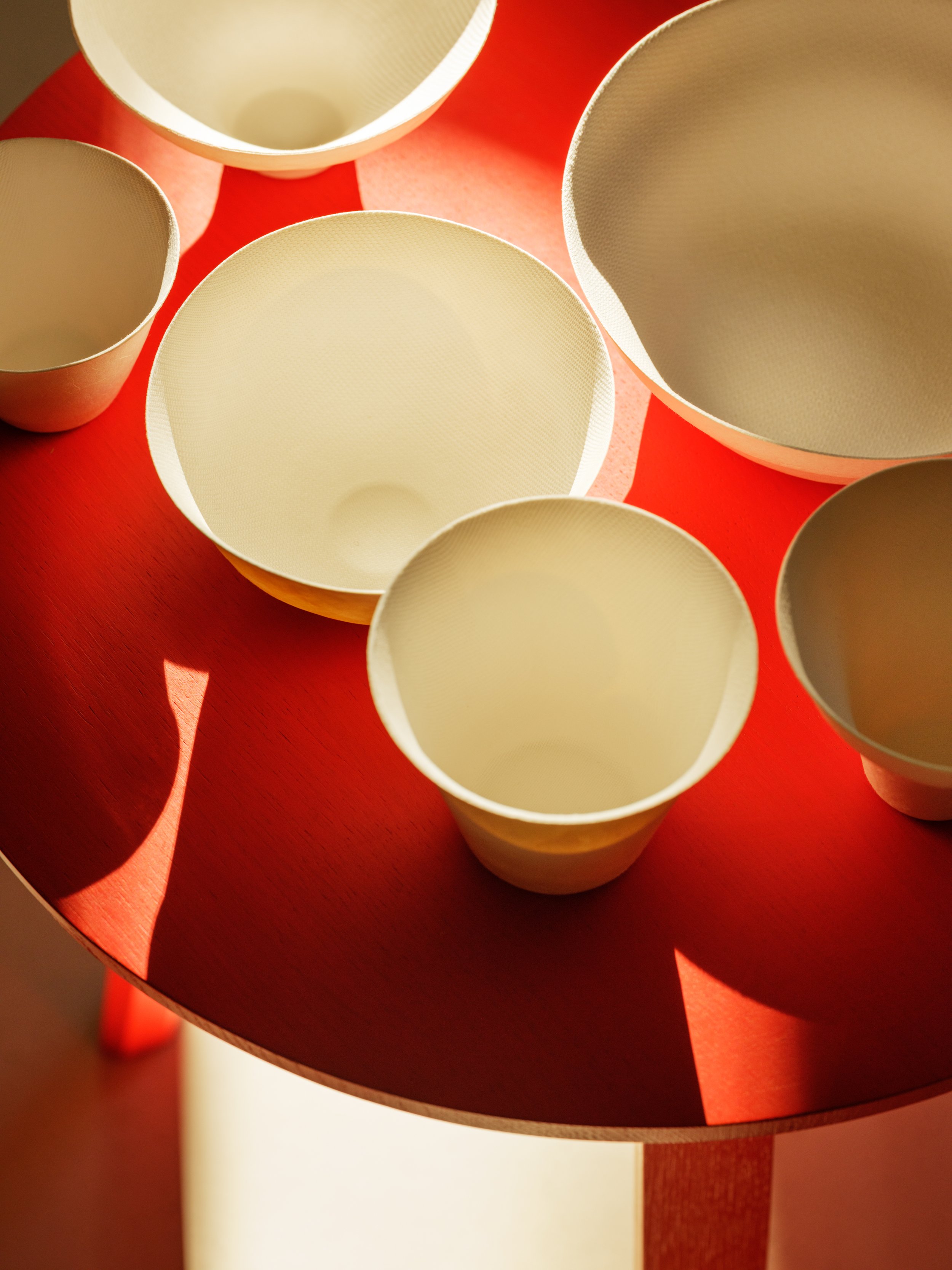 Various empty white bowls and cups on a red table with shadows.
