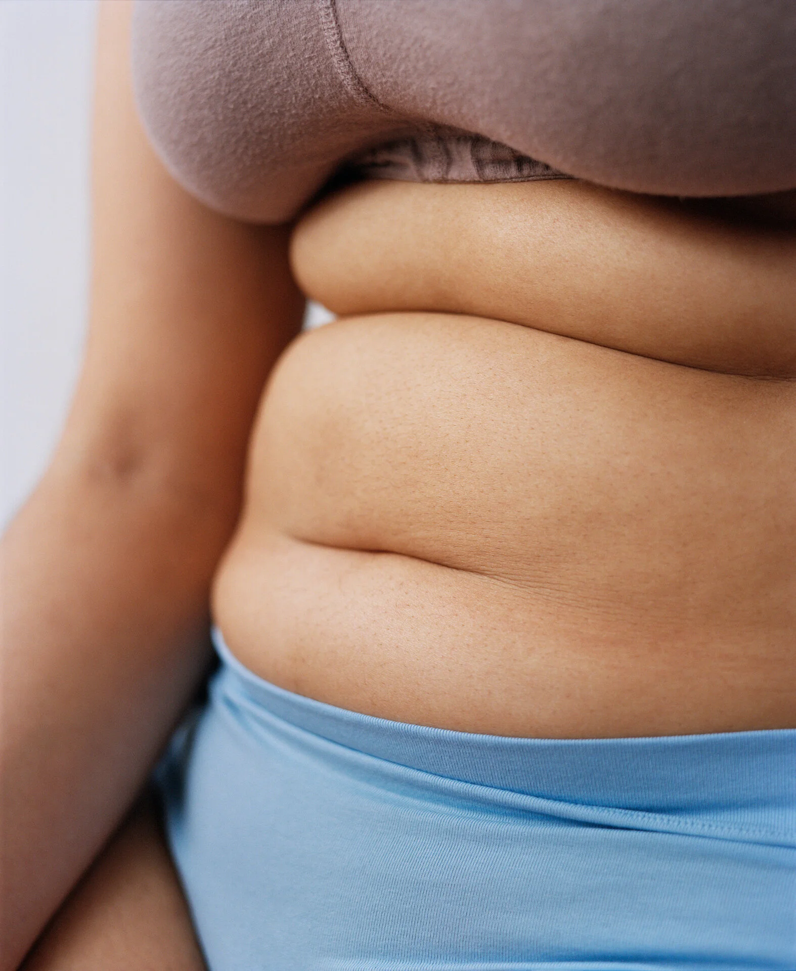Close-up of a person's midsection with visible abdominal fat, wearing a beige top and light blue underwear.