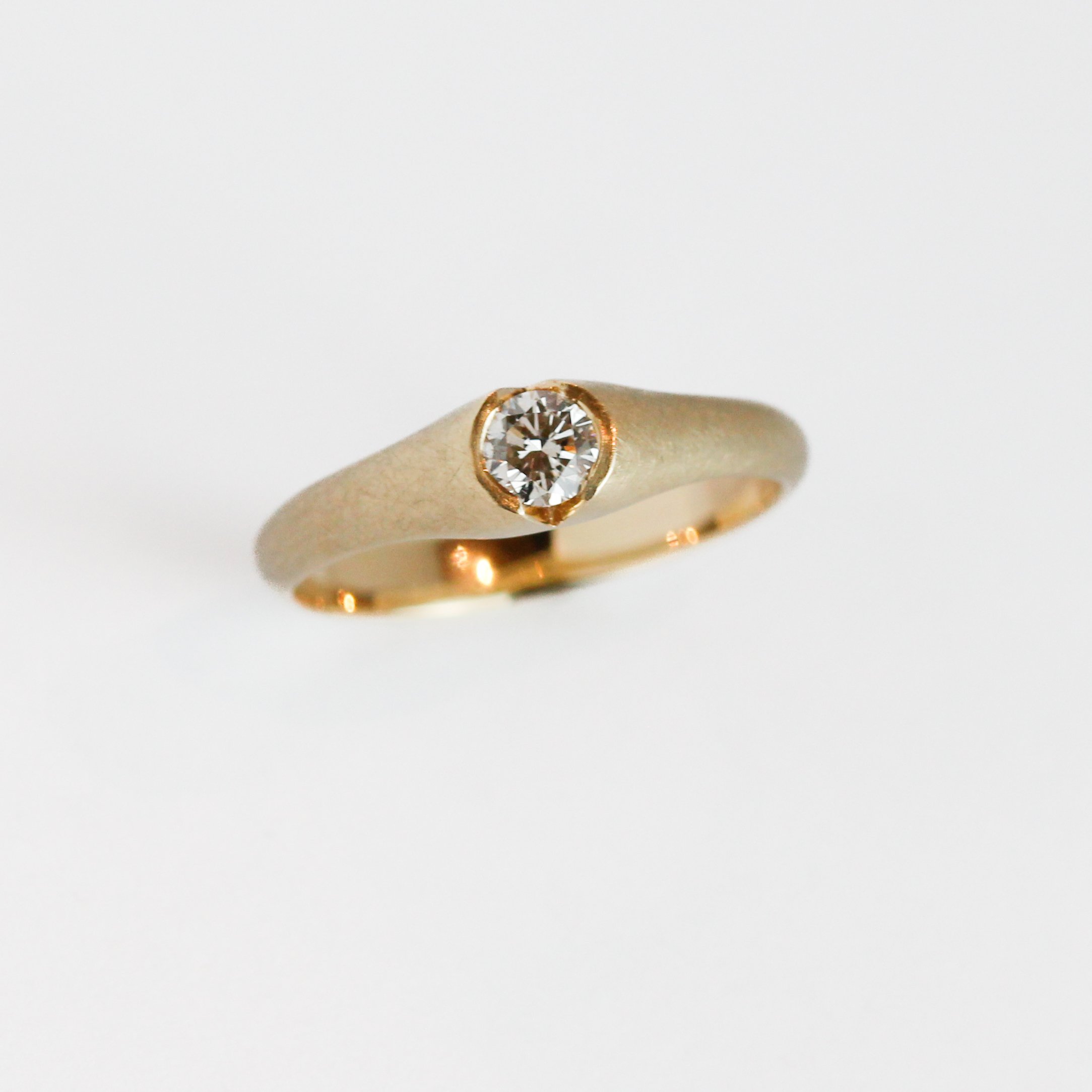 Close-up of a gold ring with a large round diamond set in a bezel setting on a white background.