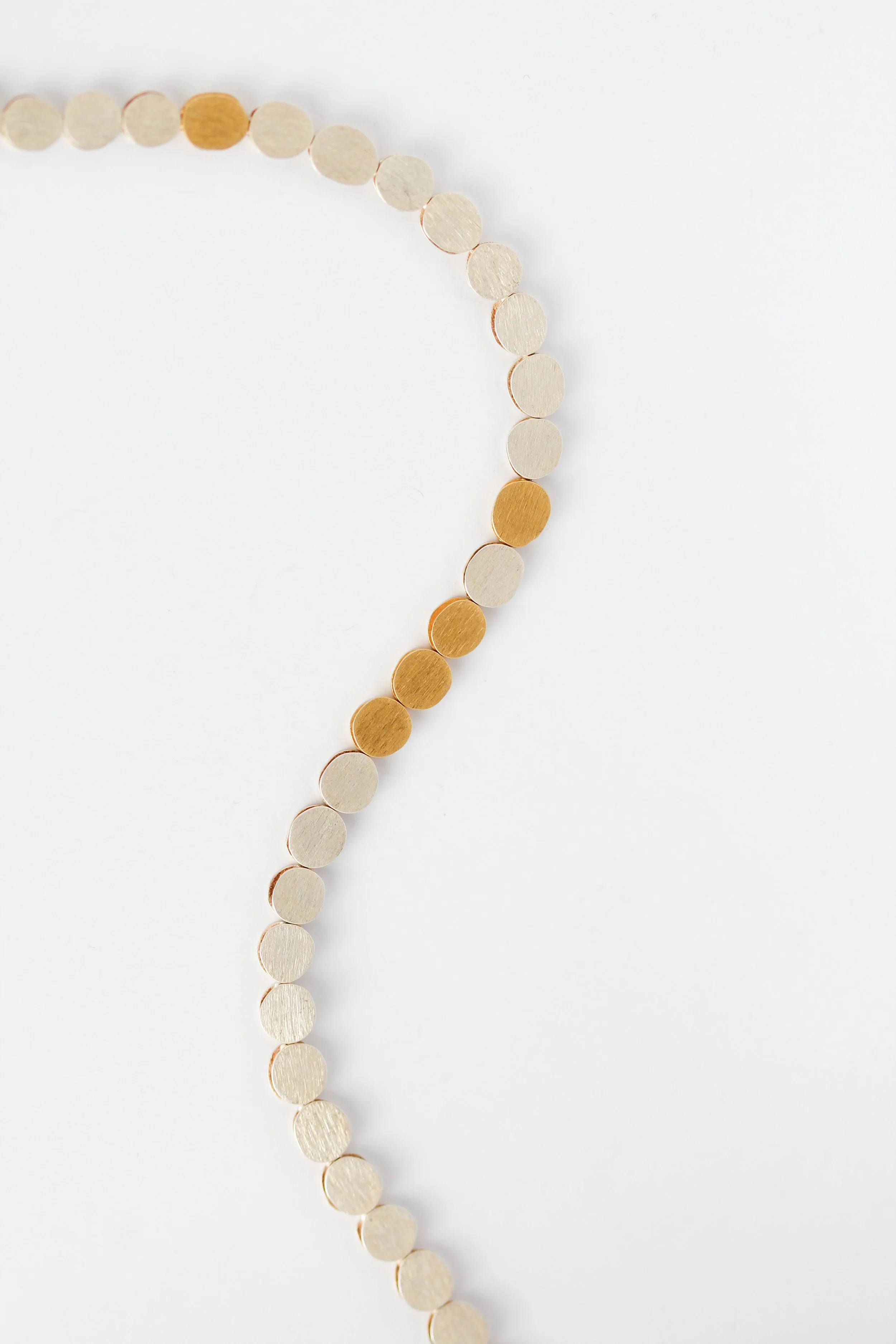 Close-up of a string of alternating gold and cream-colored circular beads on a white background.