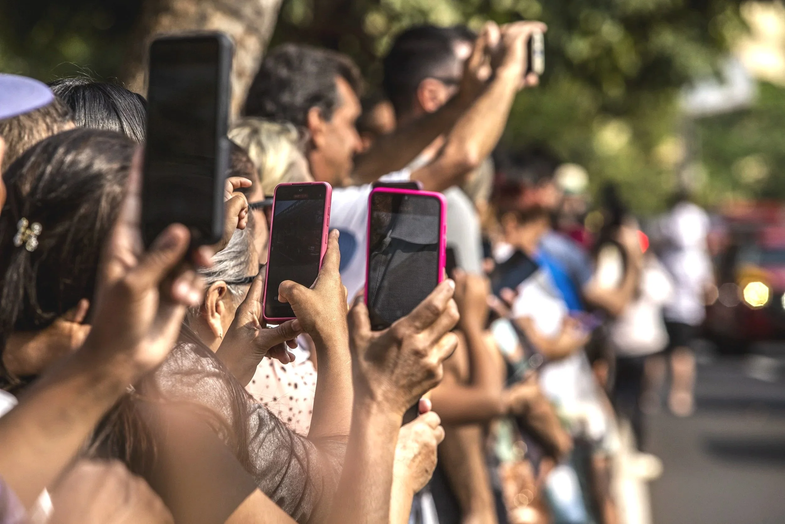 A crowd of people holding and using smartphones and cameras as they watch an outdoor event or gathering.