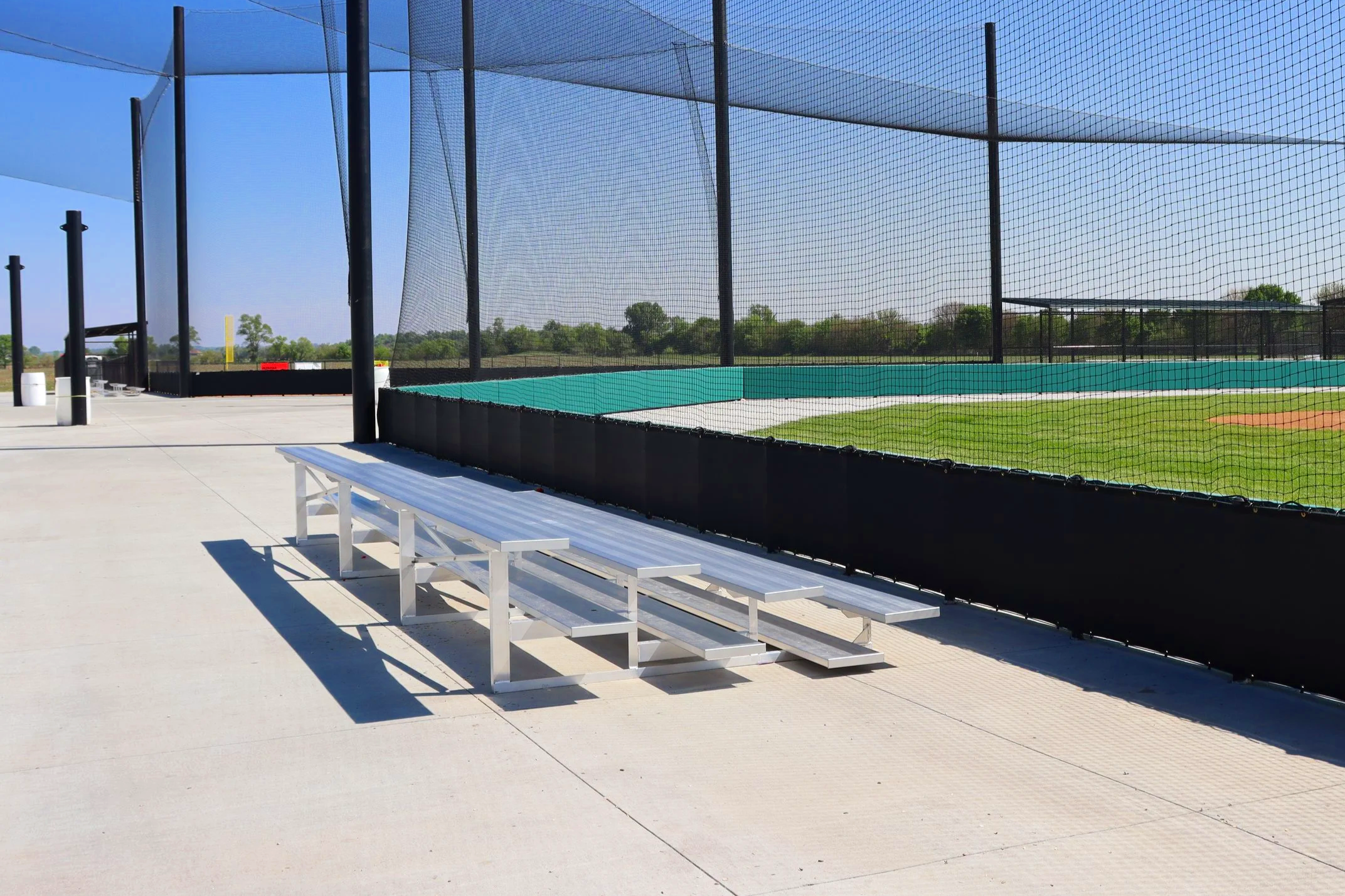 Aluminum Classic benches installed along baseball field fence line with safety netting — USS athletic facility benches supplier for Little League and youth baseball organizations