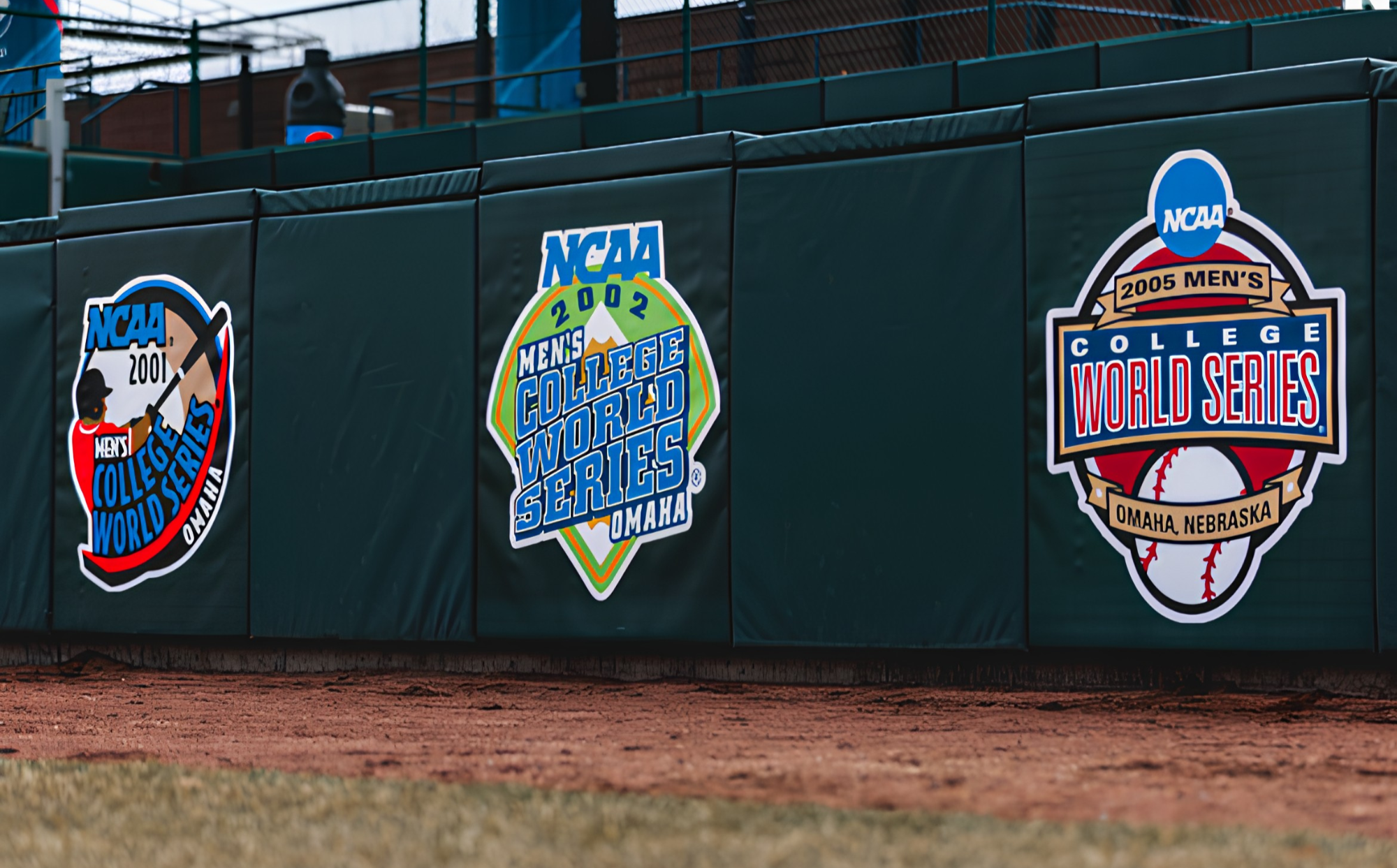 Custom branded NCAA College World Series graphics on outfield wall padding panels at Haymarket Park in Lincoln Nebraska — USS sports field padding supplier with custom athletic facility branding and graphics