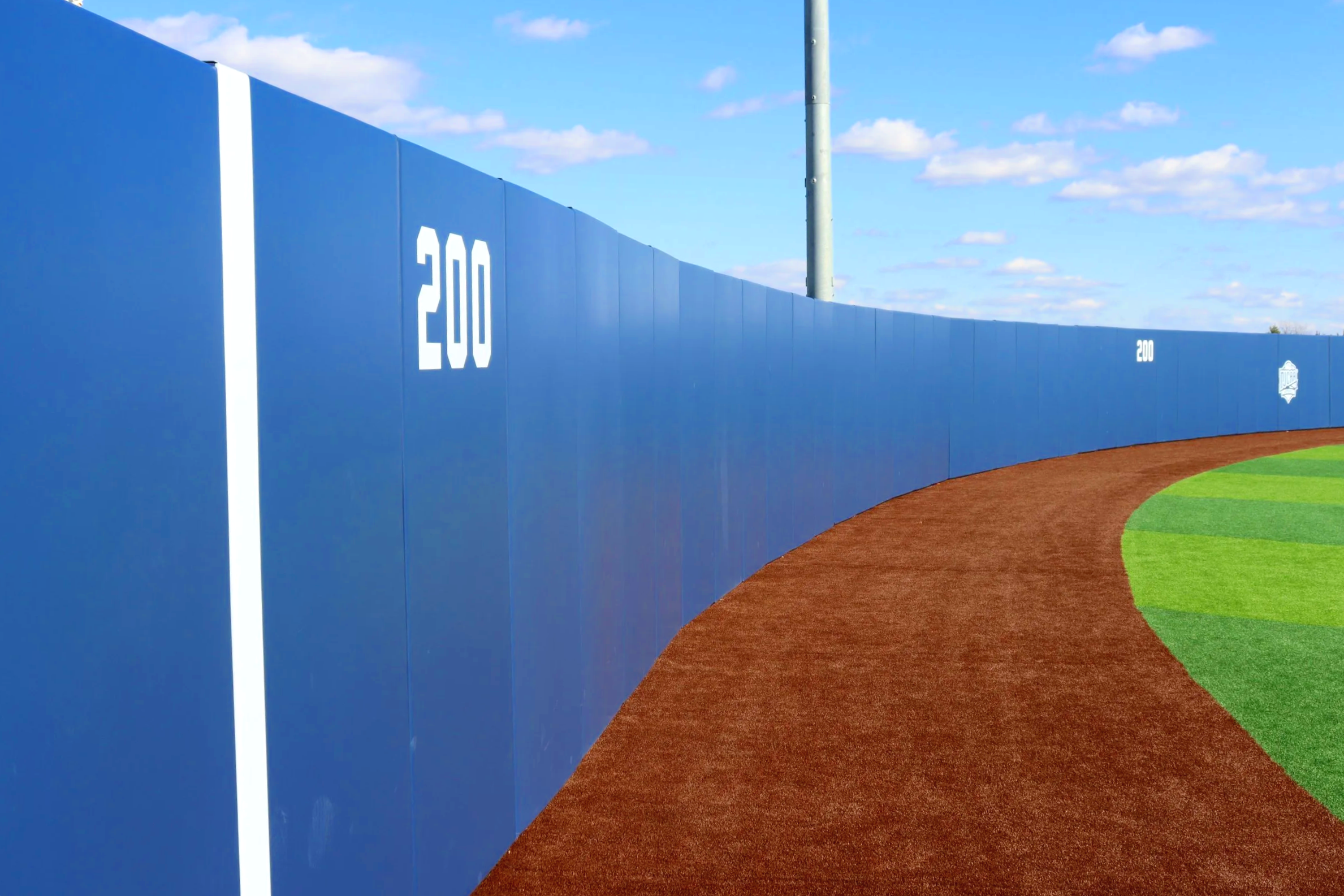 Blue exterior wall padding with distance markers along curved outfield fence at Grayson College Vikings baseball field in Texas — USS exterior wall padding supplier and sports field padding supplier protecting athletes from fence contact at every poi