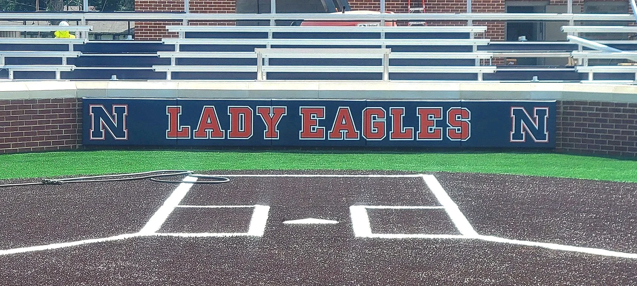 Custom branded navy blue dugout rail padding displaying Lady Eagles team name and school logo on softball baseball dugout at athletic facility — USS dugout rail padding supplier and athletic facility branding graphics supplier protecting athletes fro