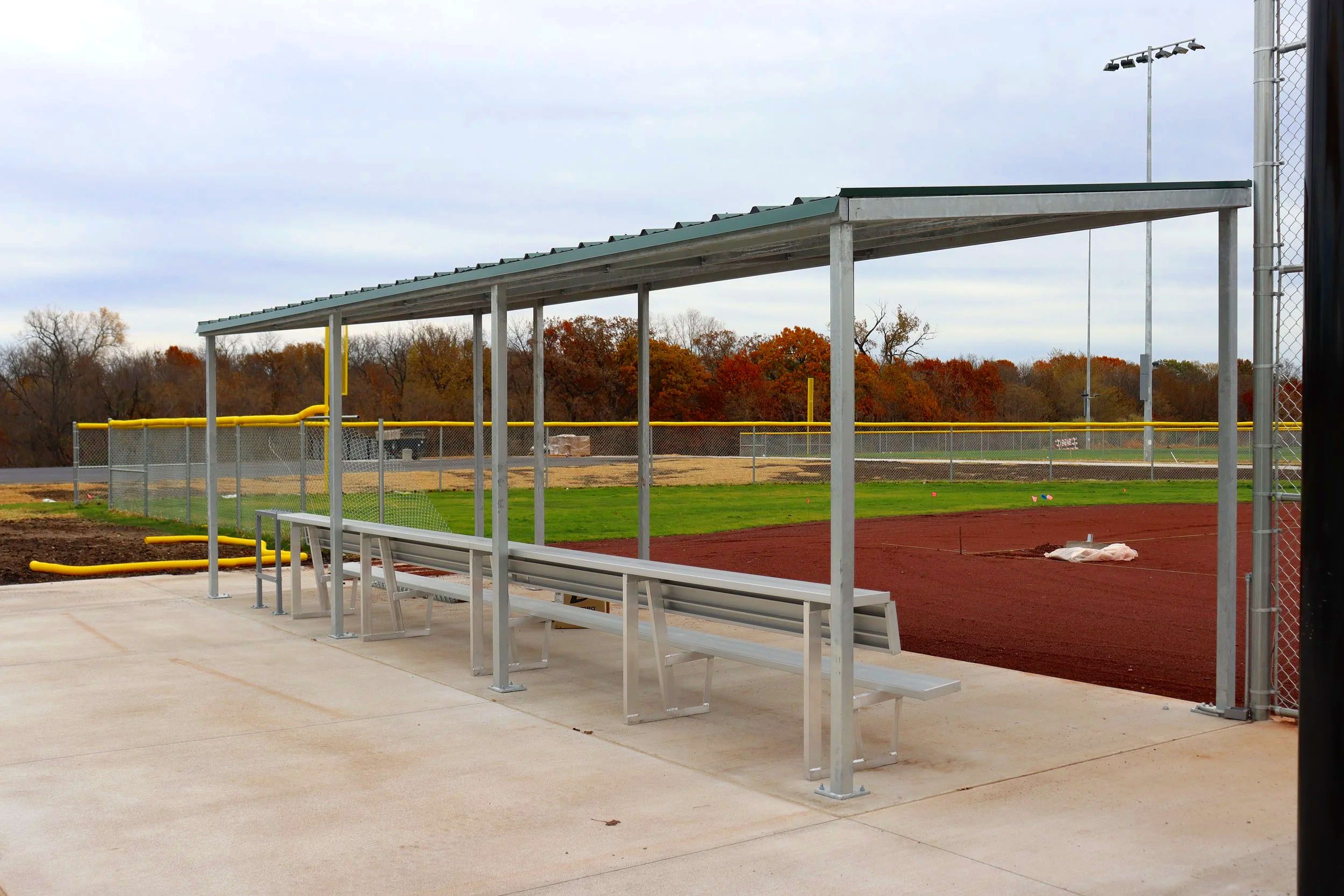 Fielder's Choice PRO baseball dugout with green metal roof aluminum bench seating and yellow foul pole at Gretna Crossing athletic facility in Gretna Nebraska — USS baseball dugout supplier