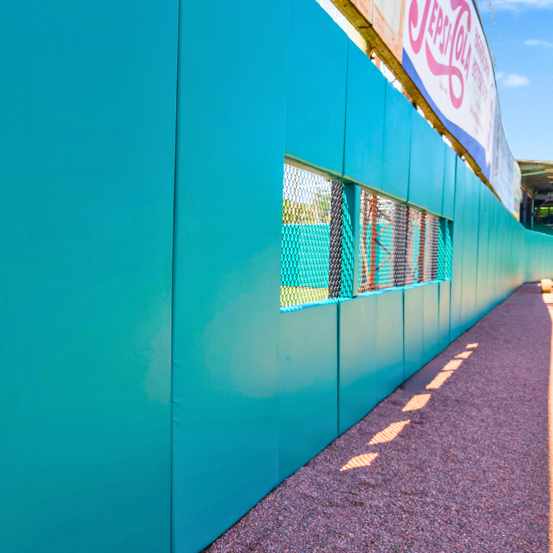 Teal outfield wall padding along warning track at Rickwood Field baseball venue in Birmingham Alabama